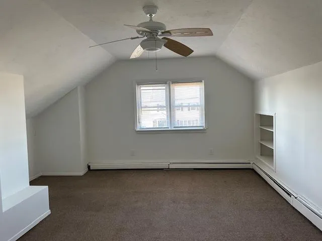 Additional living space featuring vaulted ceiling, a textured ceiling, baseboard heating, dark colored carpet, and ceiling fan Additional living space featuring vaulted ceiling, a textured ceiling, baseboard heating, dark colored carpet, and ceiling fan