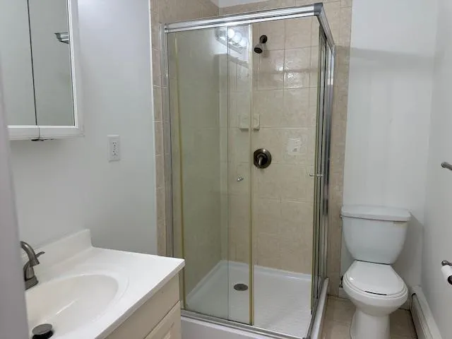 Bathroom featuring toilet, vanity, baseboard heating, and a shower stall Bathroom featuring toilet, vanity, baseboard heating, and a shower stall