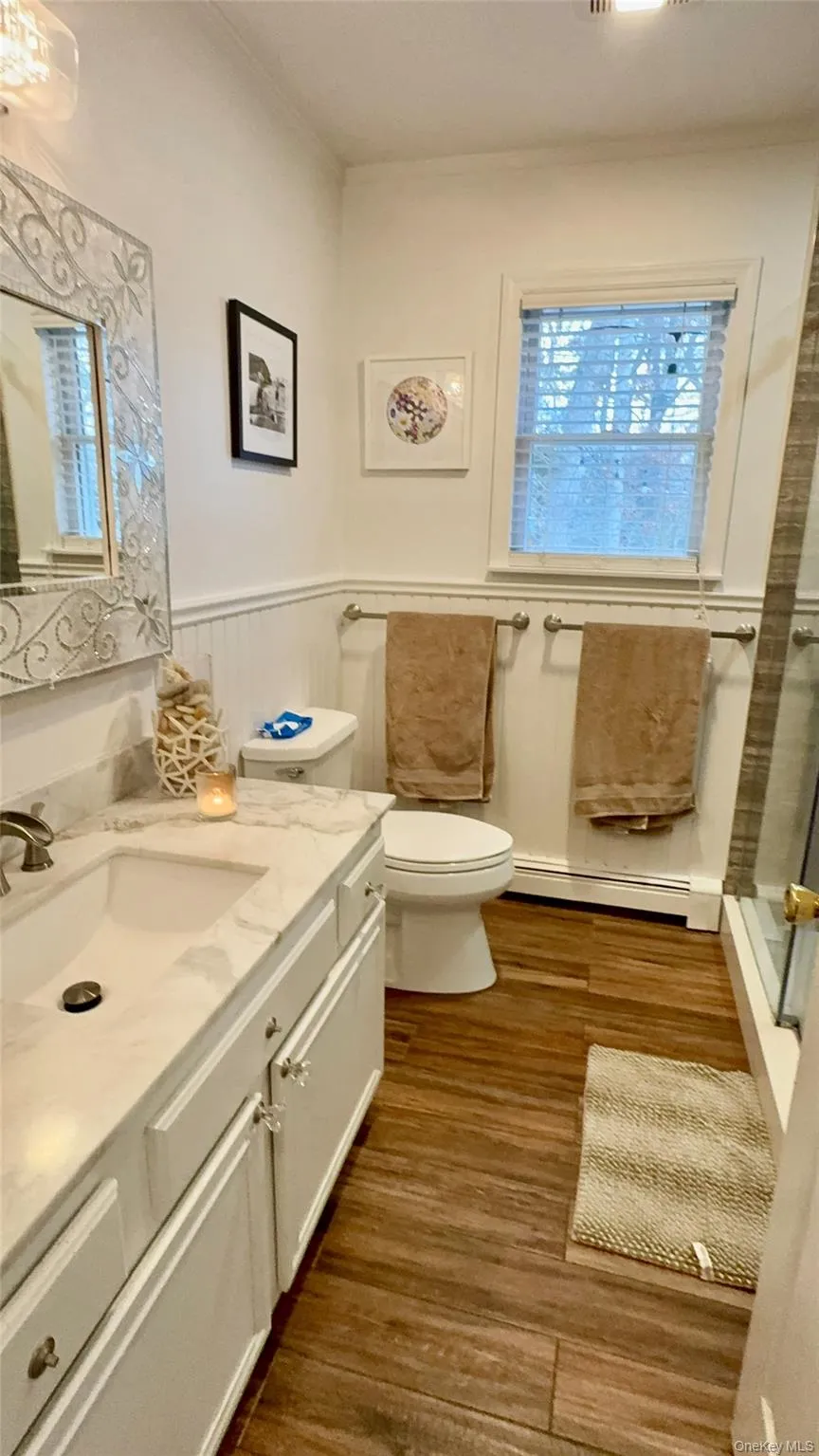 Bathroom featuring vanity, crown molding, baseboard heating, a wainscoted wall, and wood finished floors