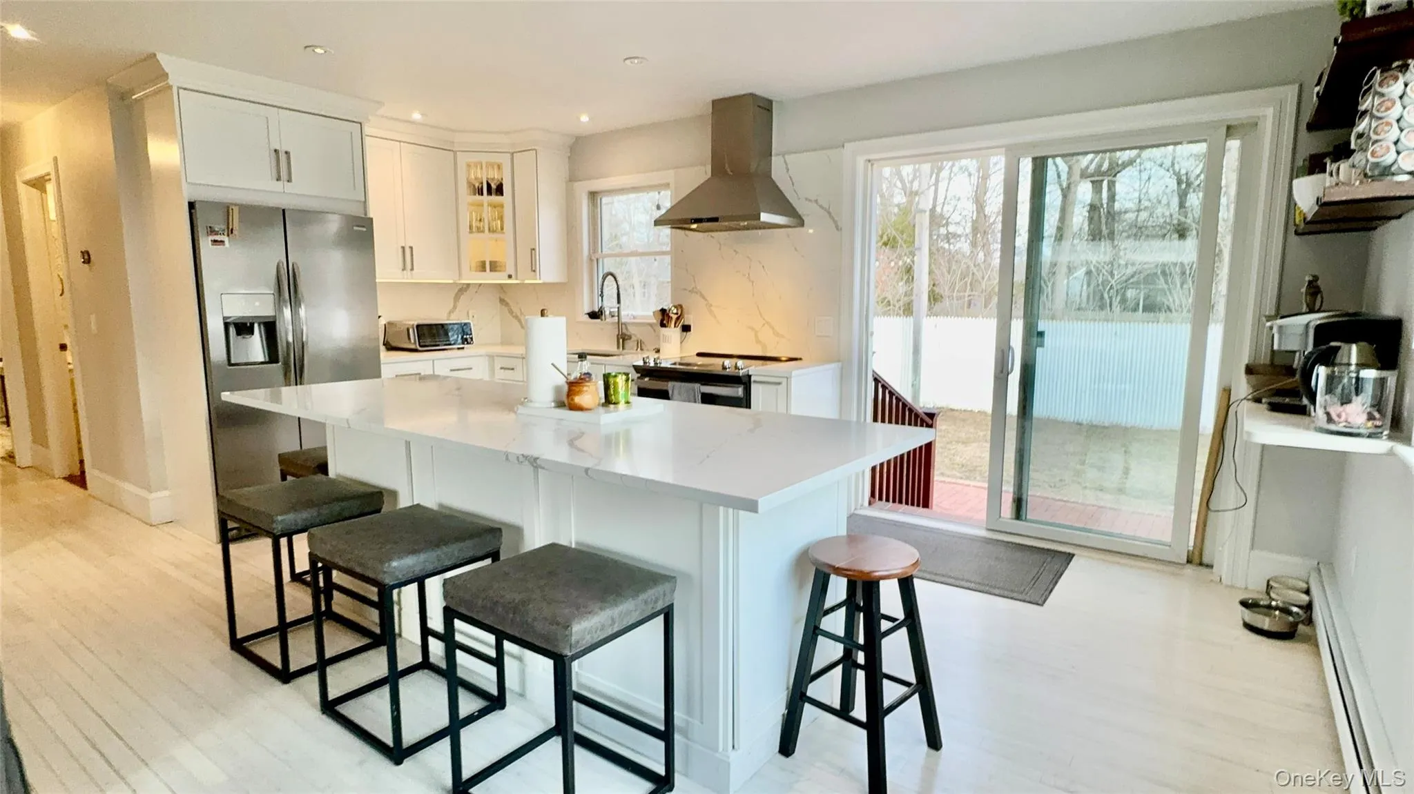Kitchen with a kitchen bar, stainless steel appliances, wall chimney exhaust hood, and light wood finished floors