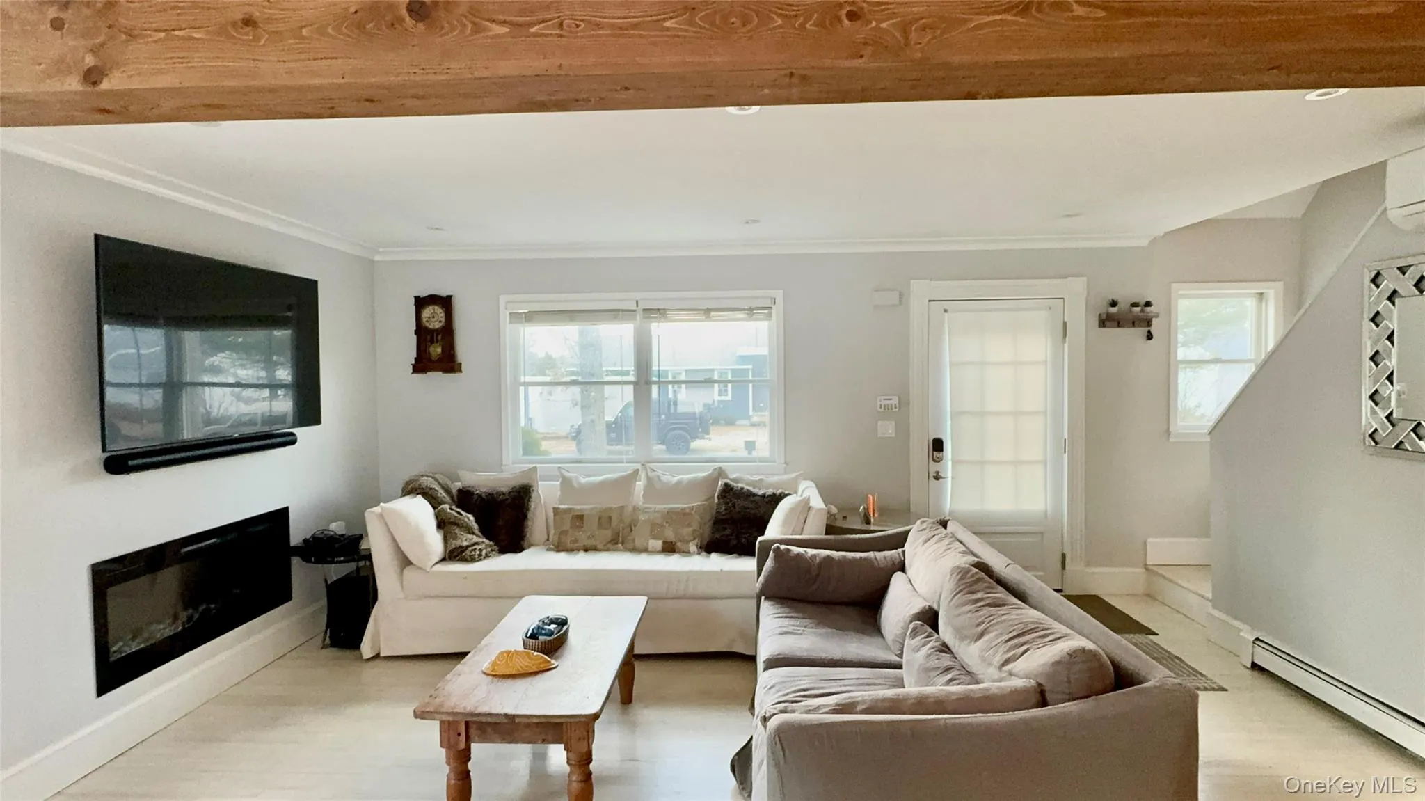 Living area featuring crown molding, a glass covered fireplace, baseboard heating, baseboards, and light wood-style floors