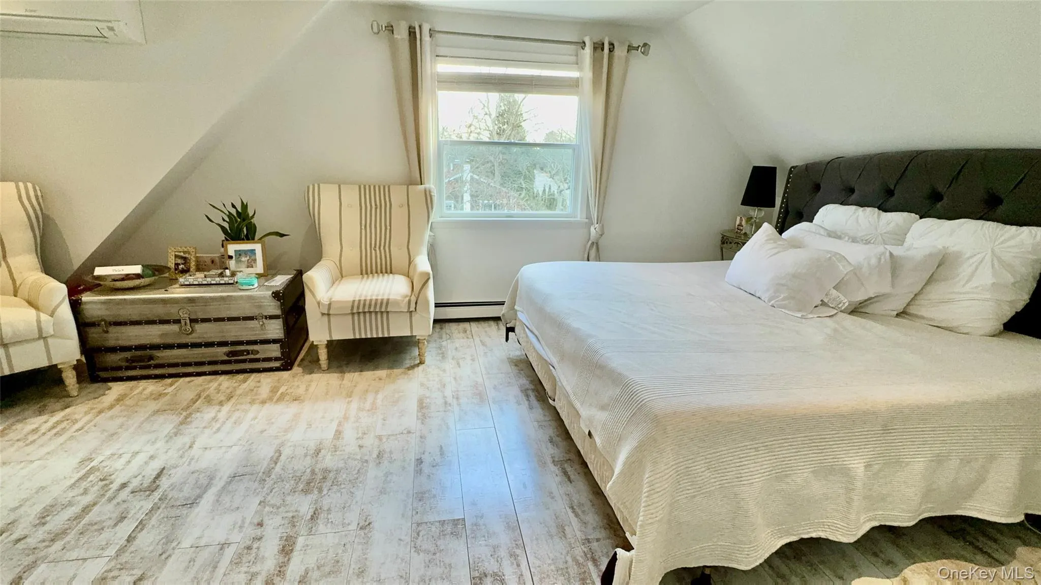 Bedroom featuring baseboard heating, wood finished floors, a wall mounted air conditioner, and vaulted ceiling