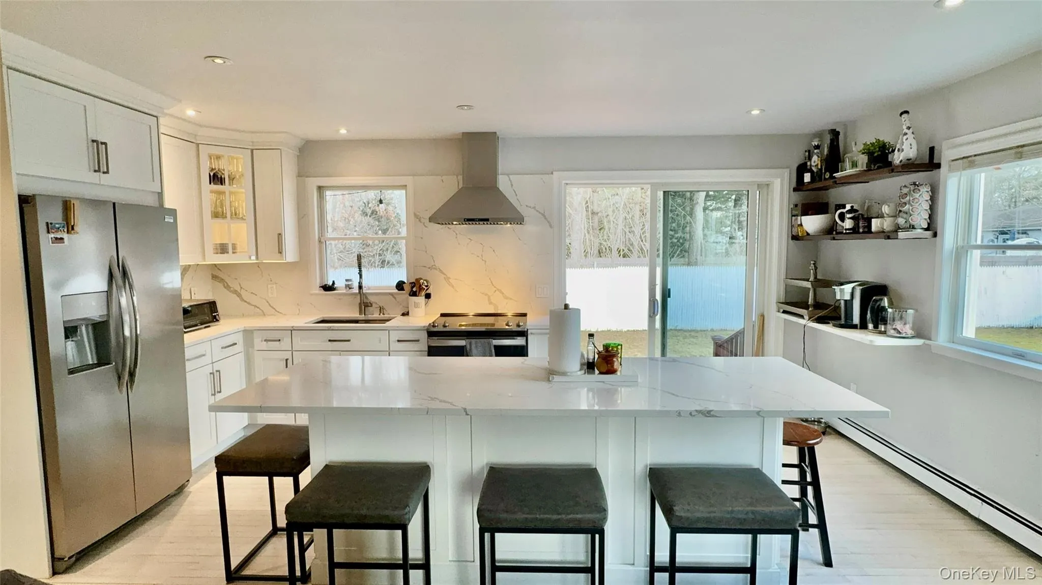 Kitchen with a sink, light wood finished floors, baseboard heating, stainless steel appliances, and wall chimney range hood