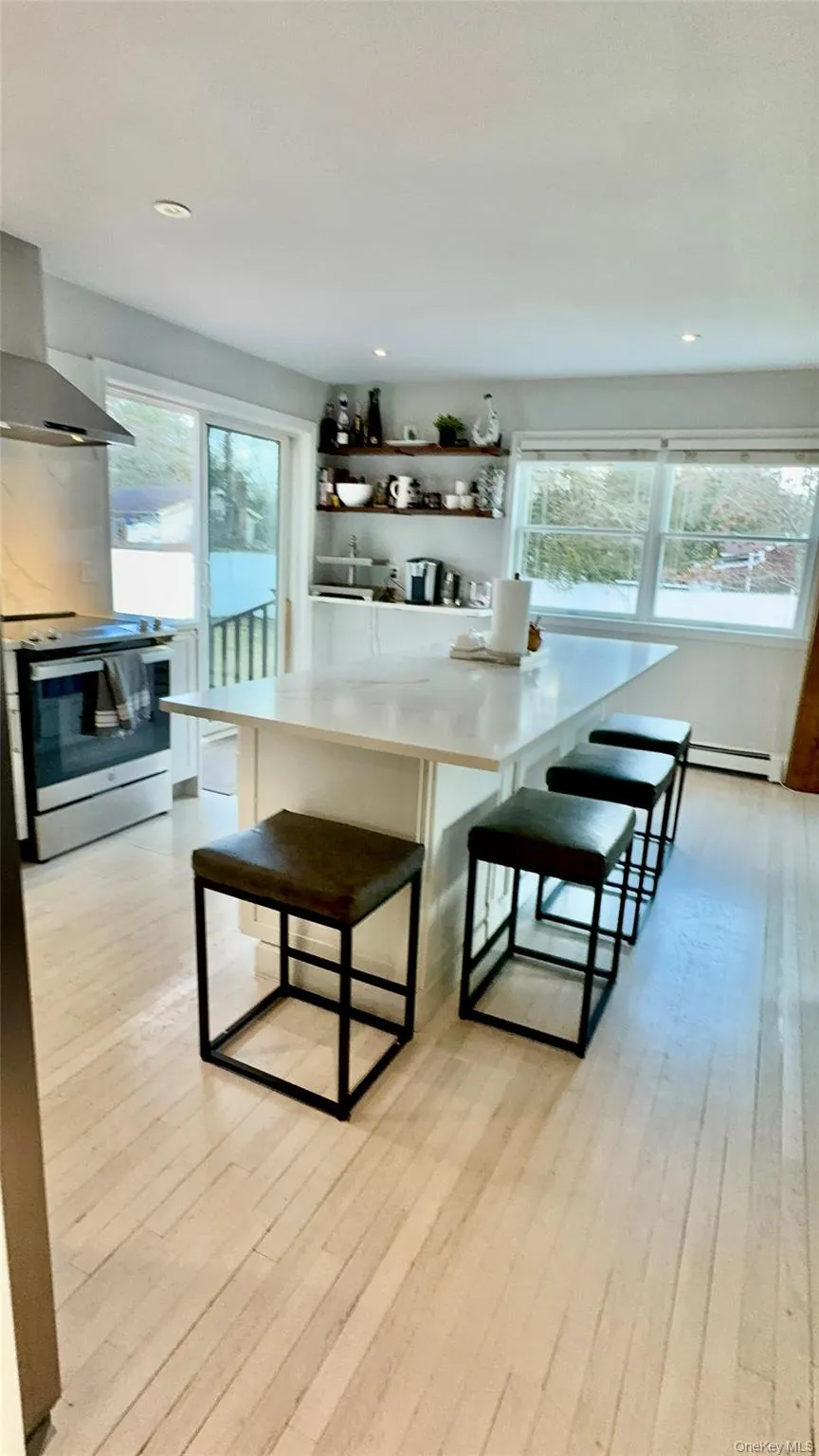 Kitchen featuring wall chimney range hood, light wood finished floors, a kitchen breakfast bar, and stainless steel electric range