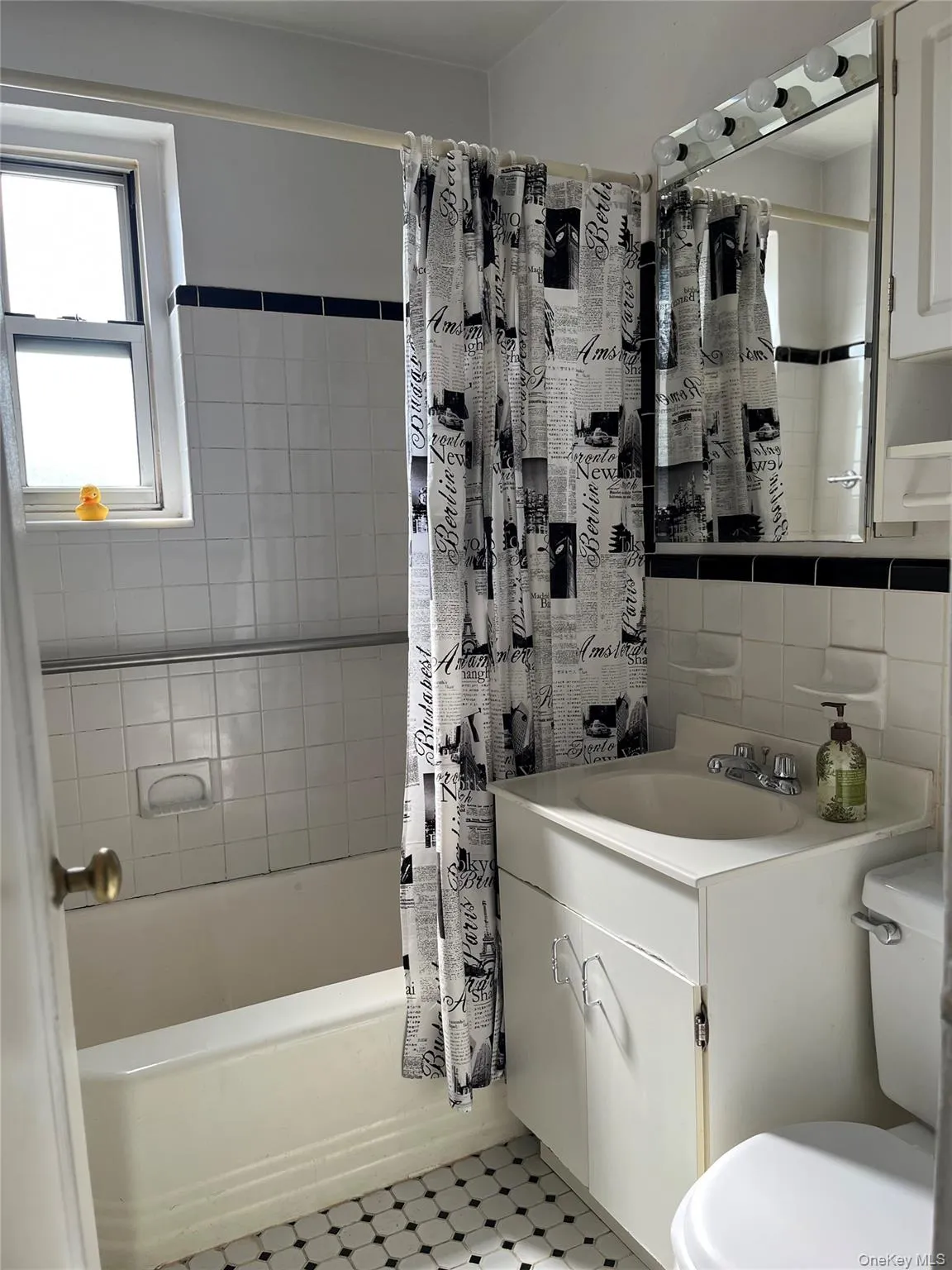 Bathroom with vanity, tile walls, toilet, tile patterned floors, and shower / bath combo Bathroom with vanity, tile walls, toilet, tile patterned floors, and shower / bath combo