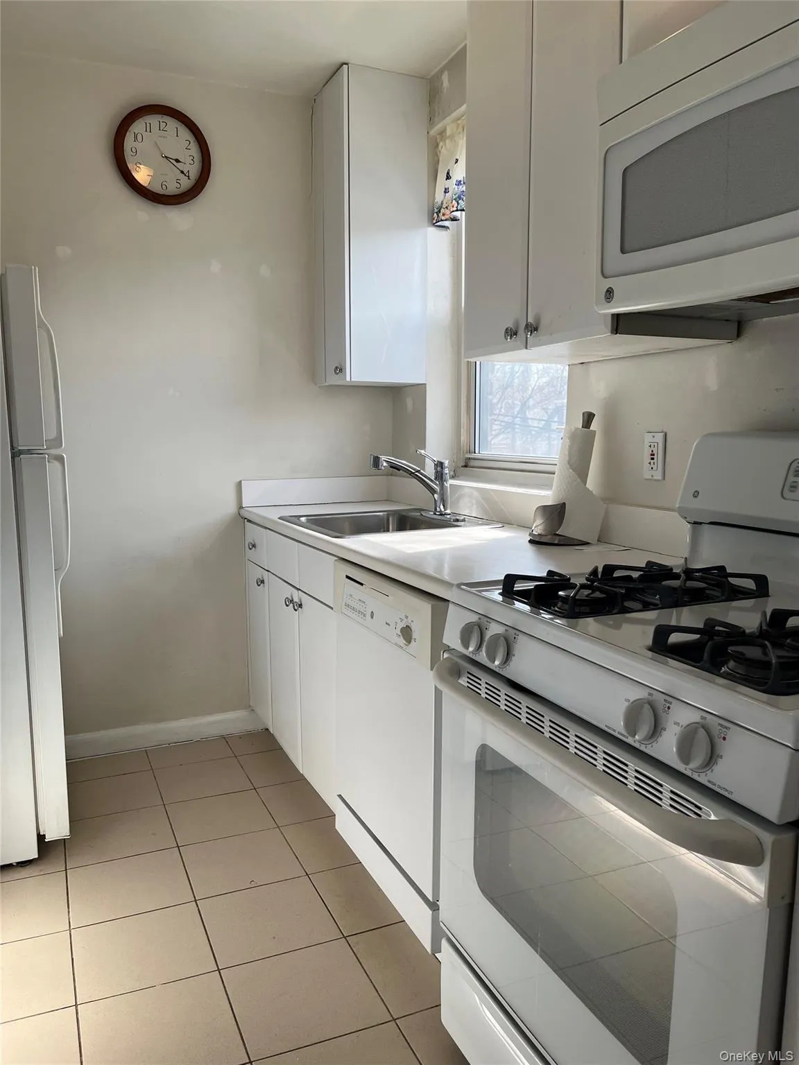 Kitchen featuring white cabinetry, a sink, light tile patterned flooring, and white appliances Kitchen featuring white cabinetry, a sink, light tile patterned flooring, and white appliances