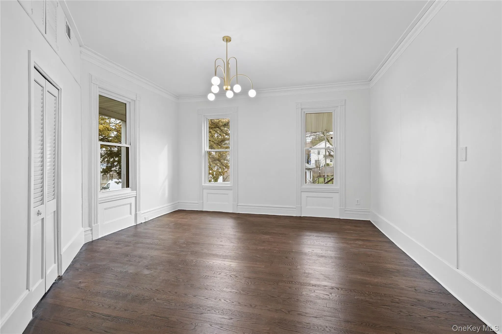Unfurnished dining area featuring crown molding, a decorative wall, a chandelier, and dark wood finished floors Unfurnished dining area featuring crown molding, a decorative wall, a chandelier, and dark wood finished floors