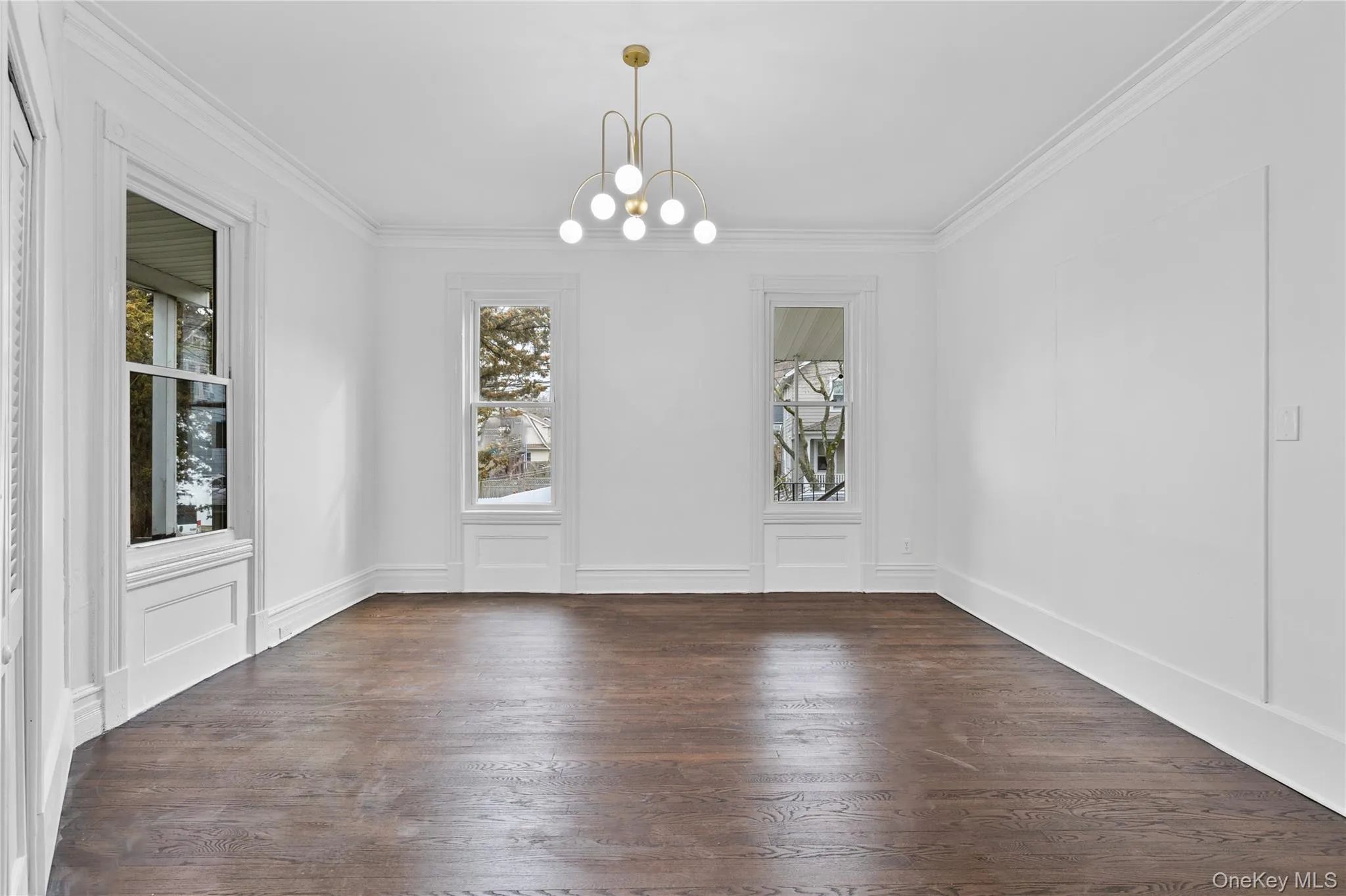 Unfurnished dining area featuring crown molding, a decorative wall, a notable chandelier, and dark wood finished floors Unfurnished dining area featuring crown molding, a decorative wall, a notable chandelier, and dark wood finished floors