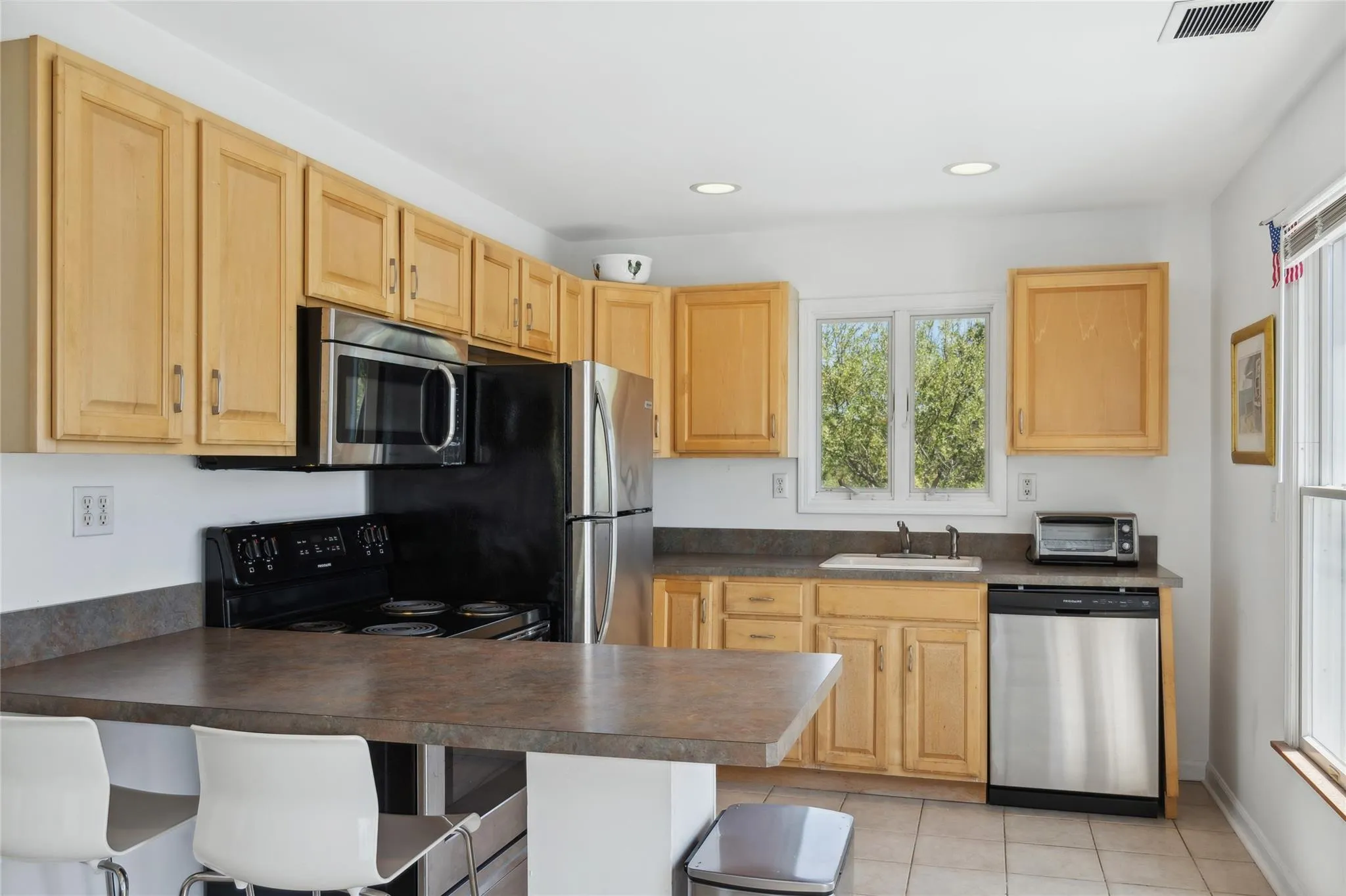 Kitchen featuring a sink, dark countertops, visible vents, light brown cabinets, and appliances with stainless steel finishes Kitchen featuring a sink, dark countertops, visible vents, light brown cabinets, and appliances with stainless steel finishes
