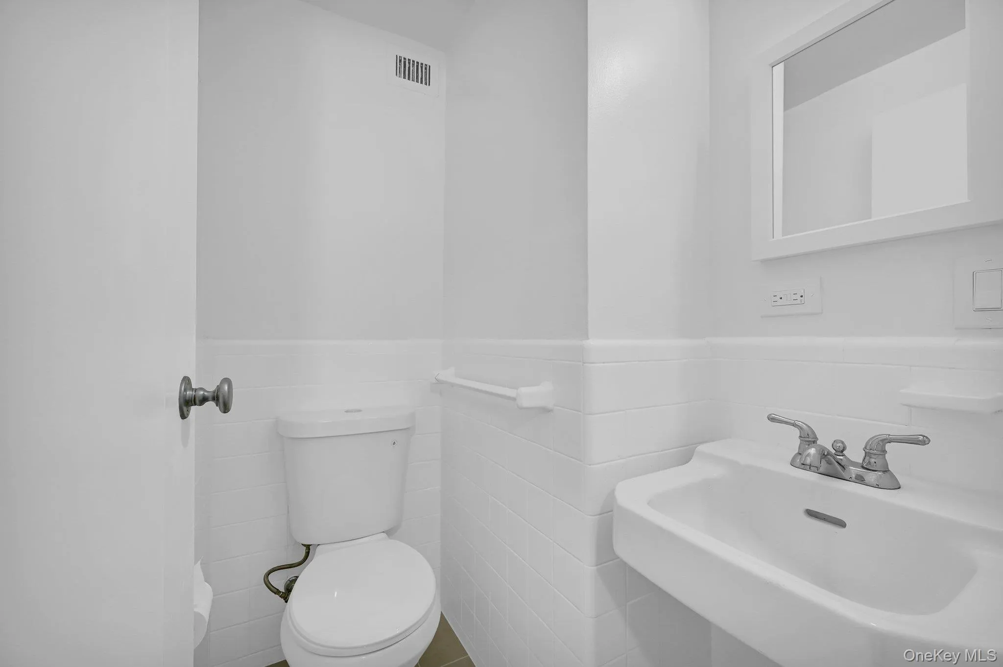 Bathroom featuring tile walls, toilet, and a sink Bathroom featuring tile walls, toilet, and a sink