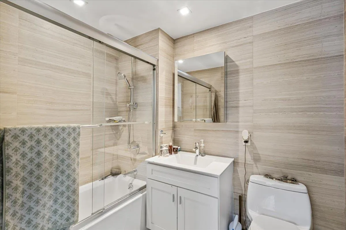 Full bath with toilet, enclosed tub / shower combo, vanity, and tile walls Full bath with toilet, enclosed tub / shower combo, vanity, and tile walls