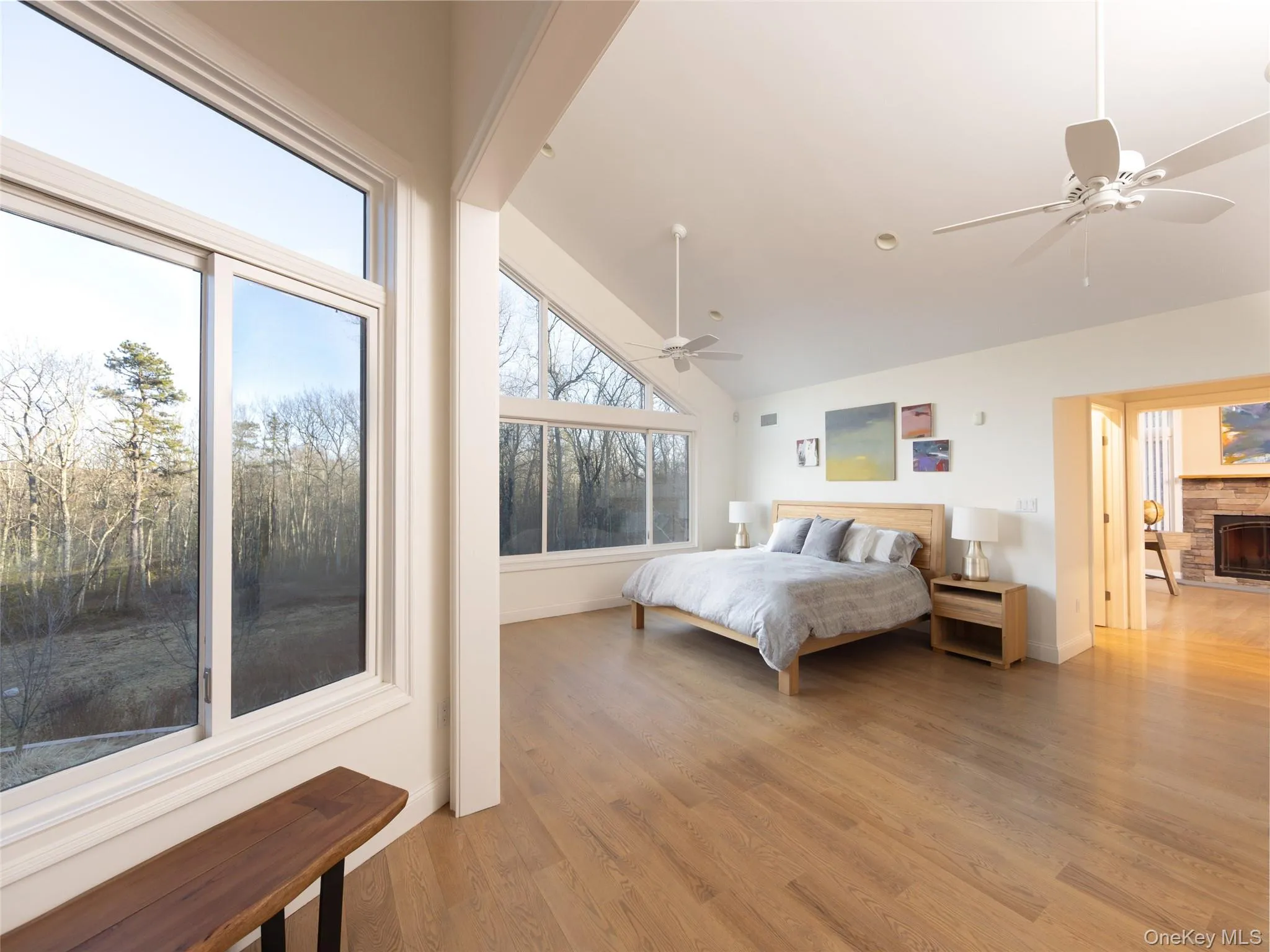 Bedroom featuring a ceiling fan, a stone fireplace, light wood finished floors, and lofted ceiling Bedroom featuring a ceiling fan, a stone fireplace, light wood finished floors, and lofted ceiling