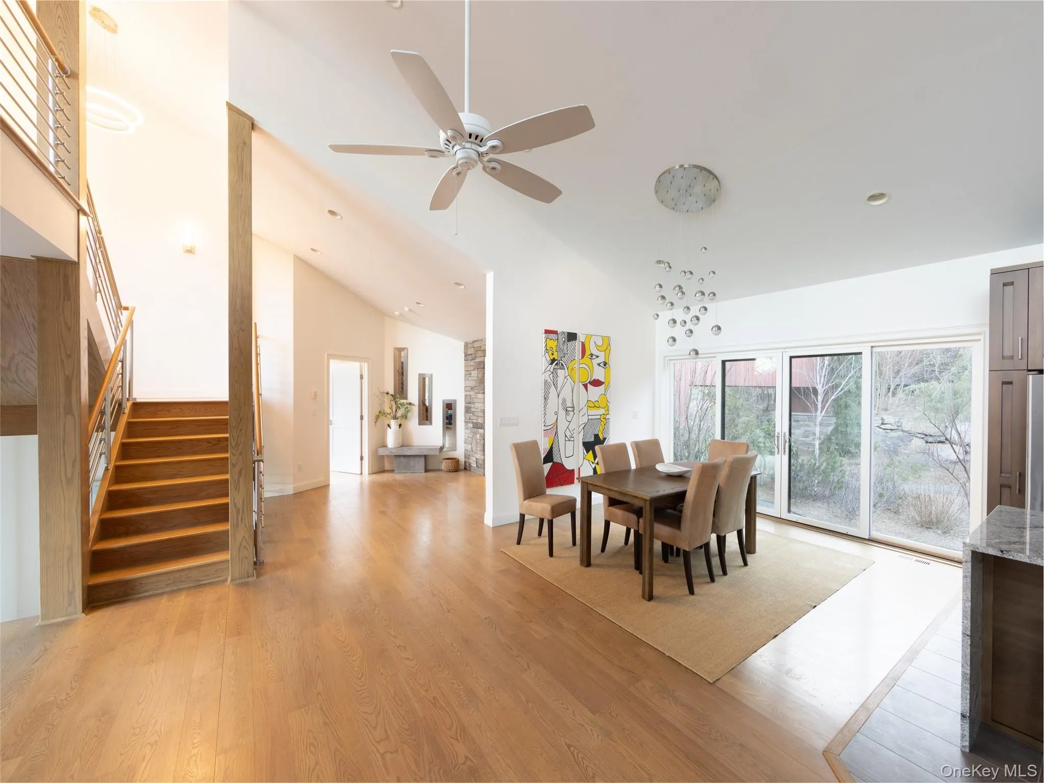 Dining room featuring light wood finished floors, high vaulted ceiling, ceiling fan, and stairs Dining room featuring light wood finished floors, high vaulted ceiling, ceiling fan, and stairs