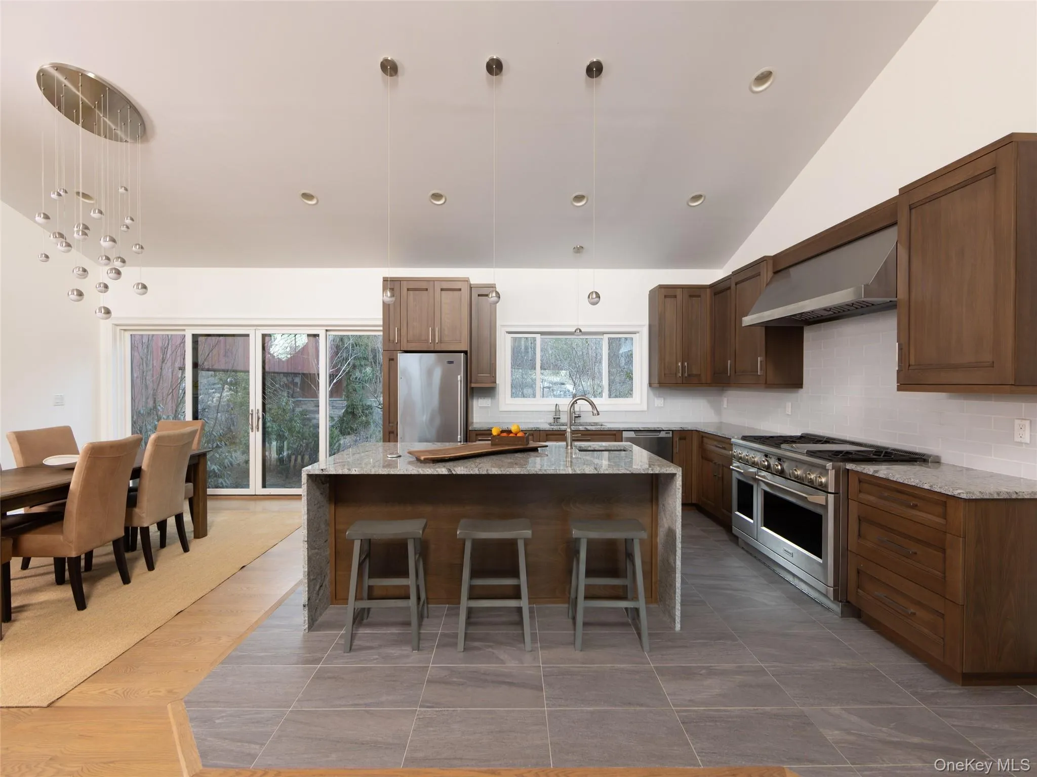 Kitchen featuring tasteful backsplash, a sink, wall chimney range hood, appliances with stainless steel finishes, and an island with sink Kitchen featuring tasteful backsplash, a sink, wall chimney range hood, appliances with stainless steel finishes, and an island with sink