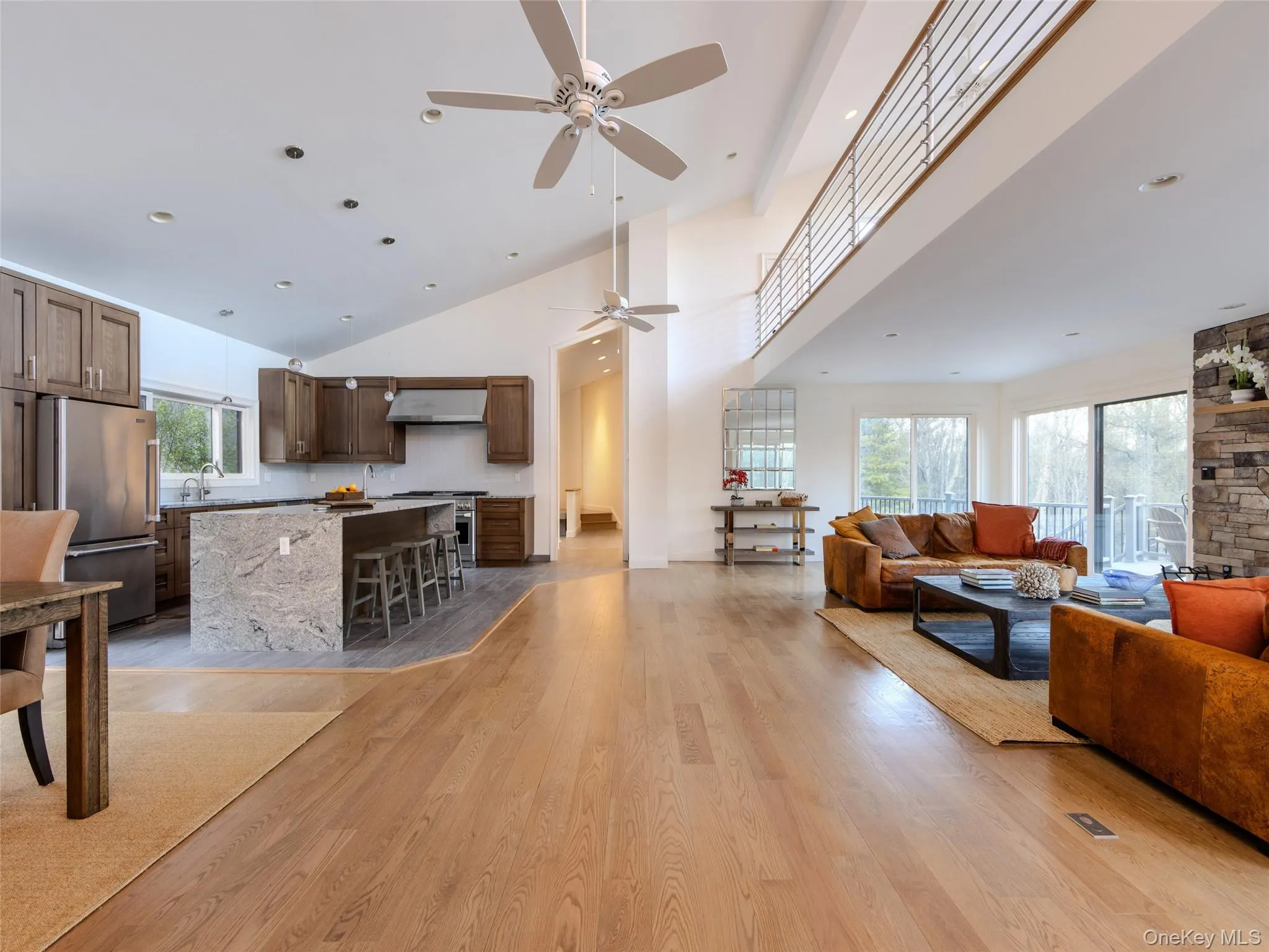 Living room featuring plenty of natural light, a towering ceiling, light wood-style flooring, and a ceiling fan Living room featuring plenty of natural light, a towering ceiling, light wood-style flooring, and a ceiling fan
