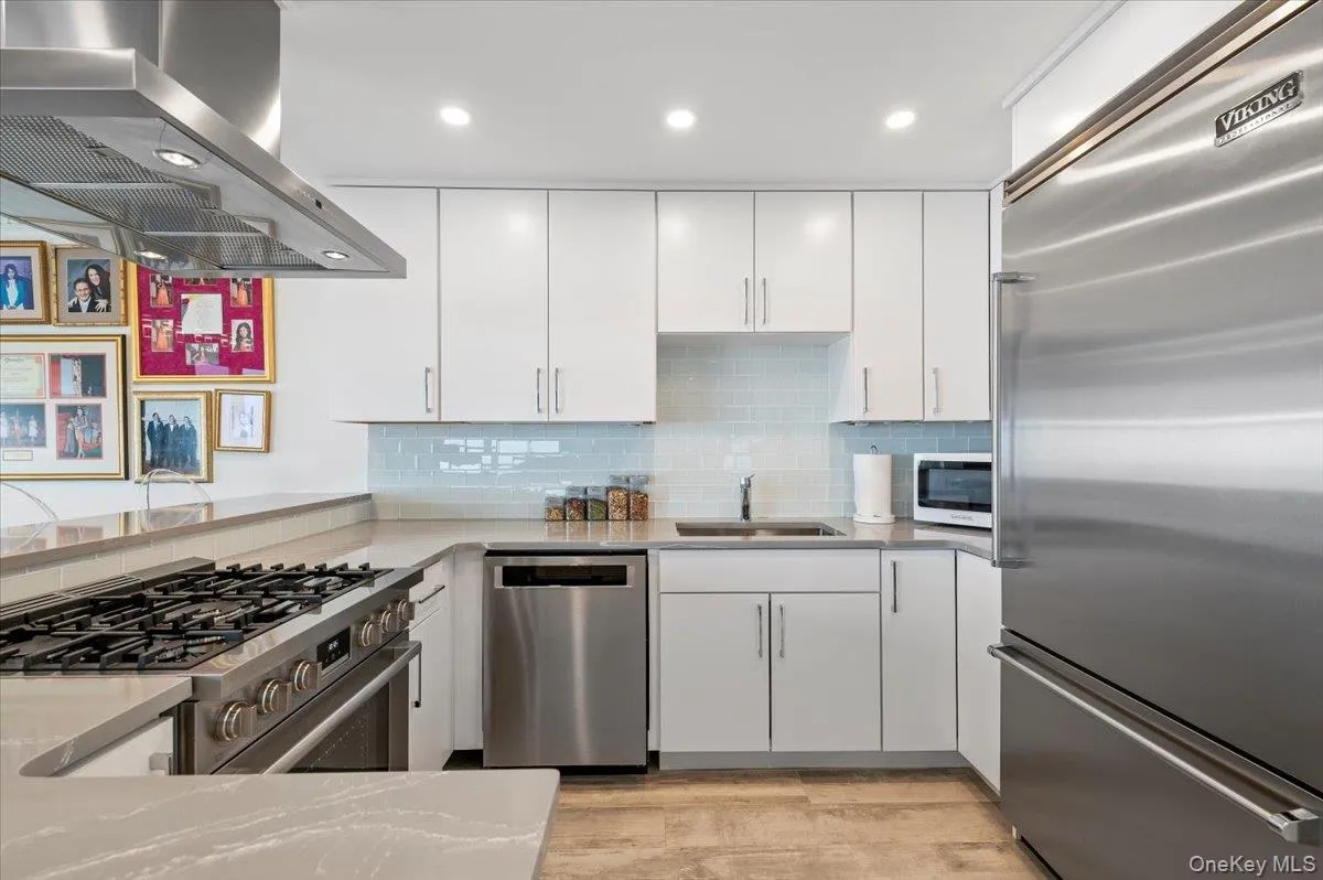 Kitchen with island range hood, backsplash, a sink, white cabinets, and appliances with stainless steel finishes Kitchen with island range hood, backsplash, a sink, white cabinets, and appliances with stainless steel finishes