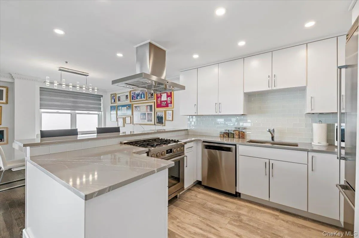 Kitchen featuring stainless steel appliances, island exhaust hood, a sink, white cabinets, and a peninsula Kitchen featuring stainless steel appliances, island exhaust hood, a sink, white cabinets, and a peninsula