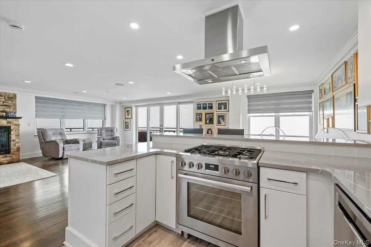 Kitchen with white cabinetry, island range hood, ornamental molding, appliances with stainless steel finishes, and a fireplace Kitchen with white cabinetry, island range hood, ornamental molding, appliances with stainless steel finishes, and a fireplace