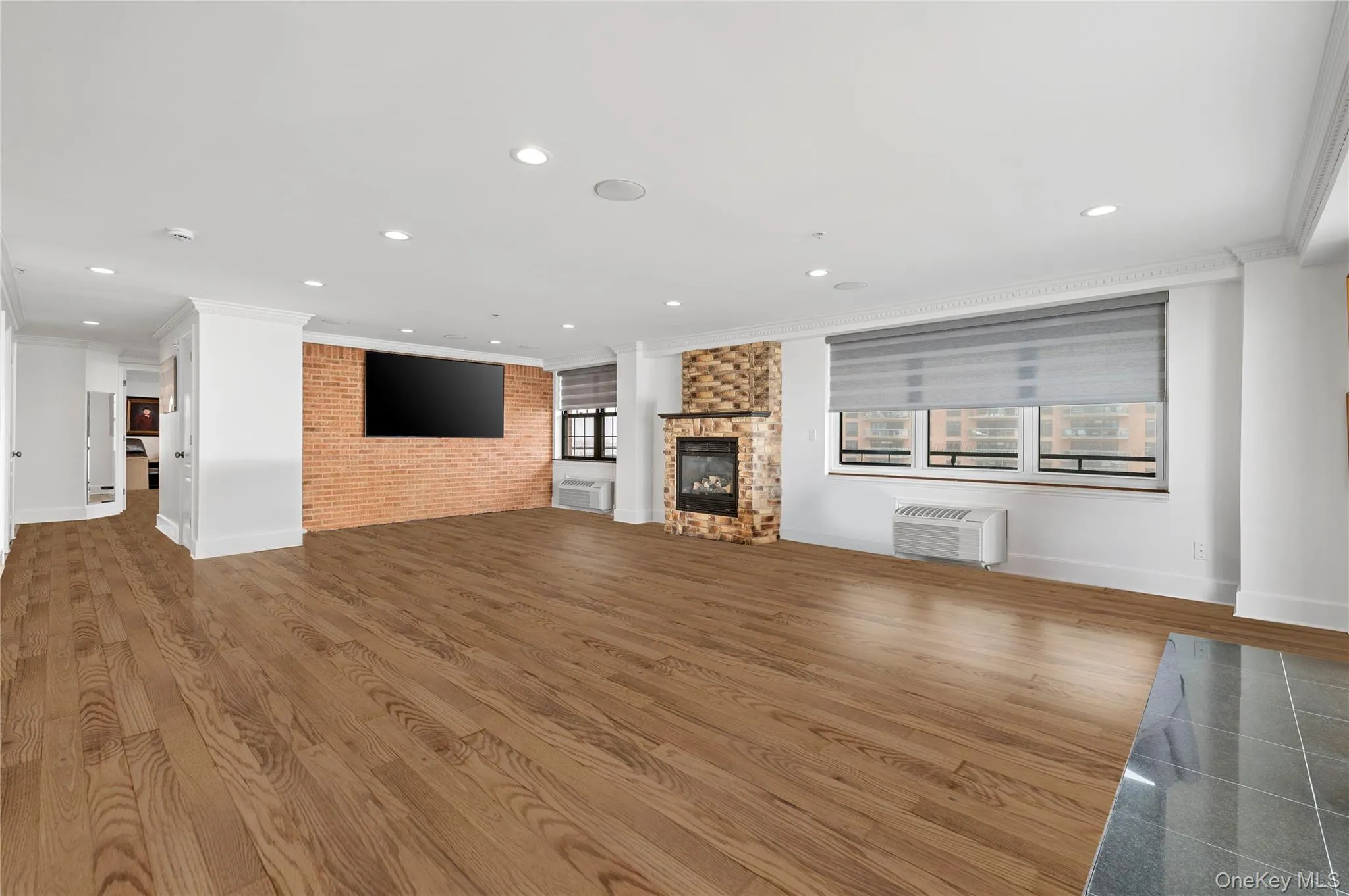 Unfurnished living room featuring a fireplace, wood finished floors, ornamental molding, and brick wall Unfurnished living room featuring a fireplace, wood finished floors, ornamental molding, and brick wall