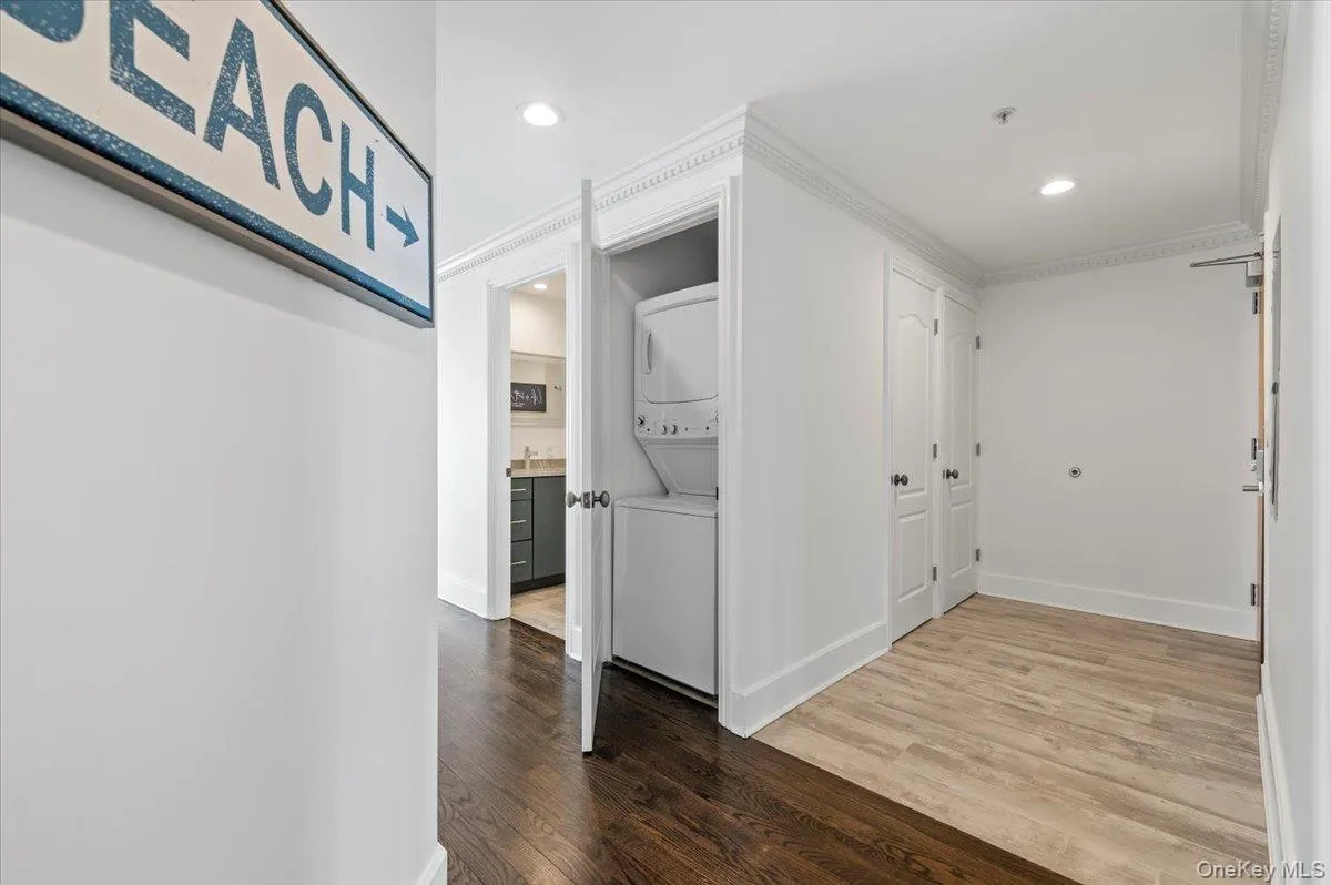 Hall with ornamental molding, wood finished floors, stacked washing maching and dryer, and recessed lighting Hall with ornamental molding, wood finished floors, stacked washing maching and dryer, and recessed lighting