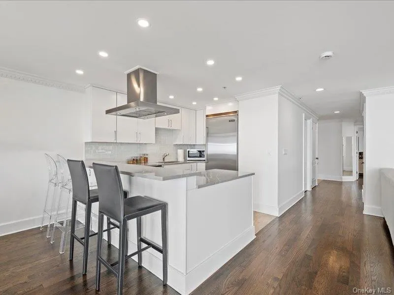 Kitchen featuring tasteful backsplash, appliances with stainless steel finishes, a peninsula, island range hood, and white cabinets Kitchen featuring tasteful backsplash, appliances with stainless steel finishes, a peninsula, island range hood, and white cabinets