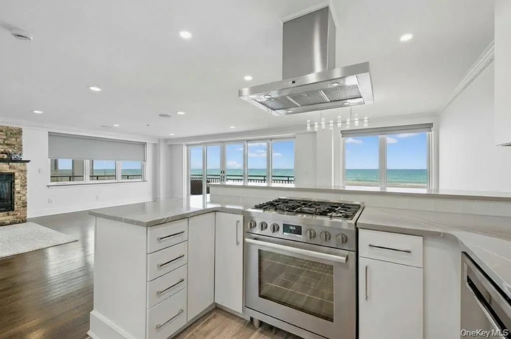 Kitchen featuring stainless steel appliances, white cabinetry, island exhaust hood, light wood-type flooring, and ornamental molding Kitchen featuring stainless steel appliances, white cabinetry, island exhaust hood, light wood-type flooring, and ornamental molding
