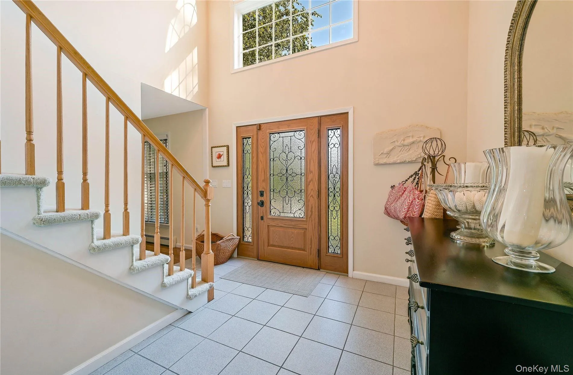 Entrance foyer featuring a towering ceiling, stairs, light tile patterned floors, baseboards, and a baseboard heating unit Entrance foyer featuring a towering ceiling, stairs, light tile patterned floors, baseboards, and a baseboard heating unit