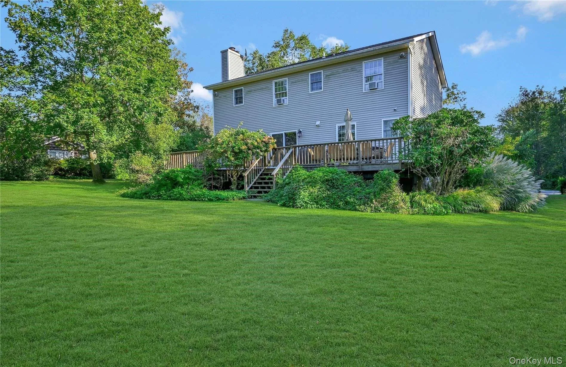 Back of house featuring a chimney, a deck, and a lawn Back of house featuring a chimney, a deck, and a lawn