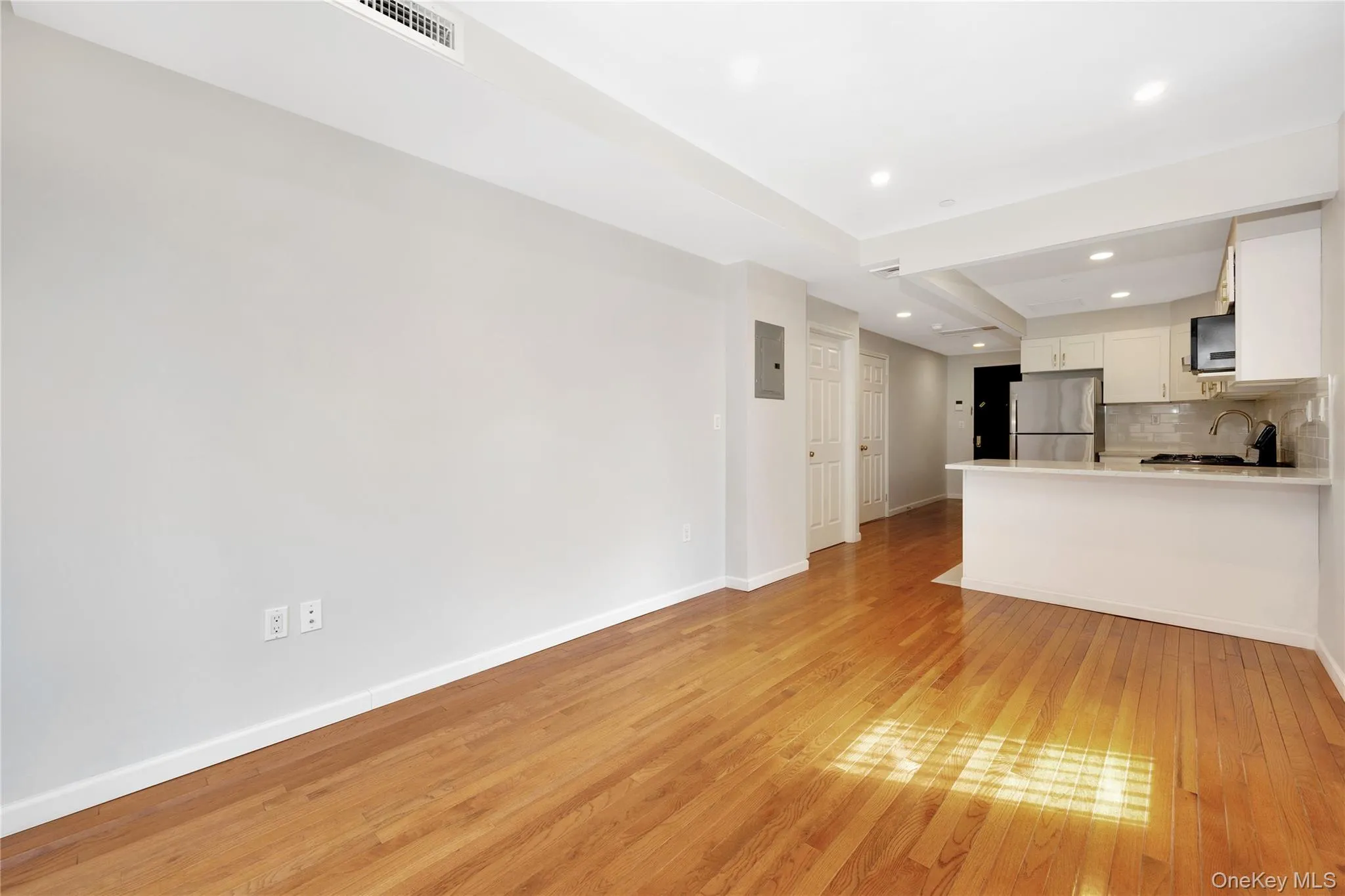 Kitchen with tasteful backsplash, white cabinetry, freestanding refrigerator, light wood-style floors, and a sink Kitchen with tasteful backsplash, white cabinetry, freestanding refrigerator, light wood-style floors, and a sink