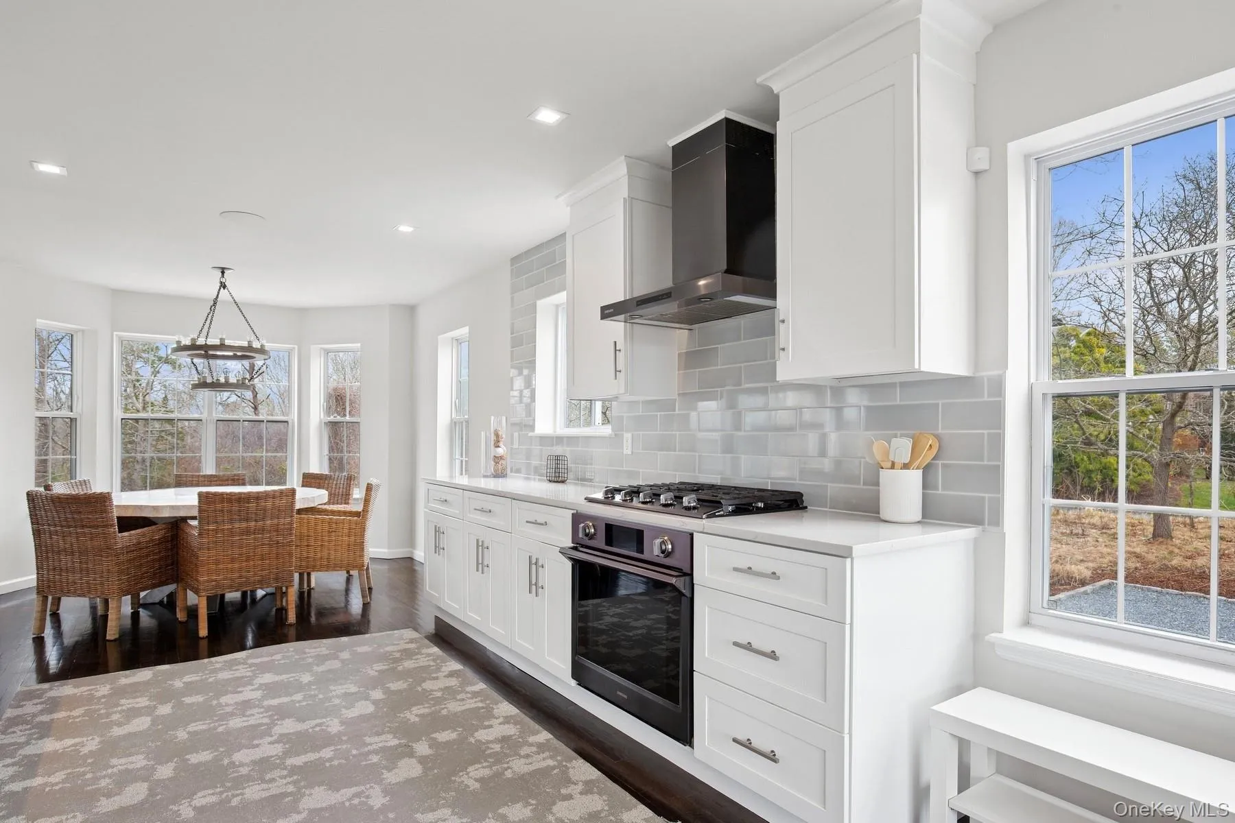 Kitchen with wall chimney range hood, stainless steel gas cooktop, black oven, decorative backsplash, and dark wood-style floors Kitchen with wall chimney range hood, stainless steel gas cooktop, black oven, decorative backsplash, and dark wood-style floors