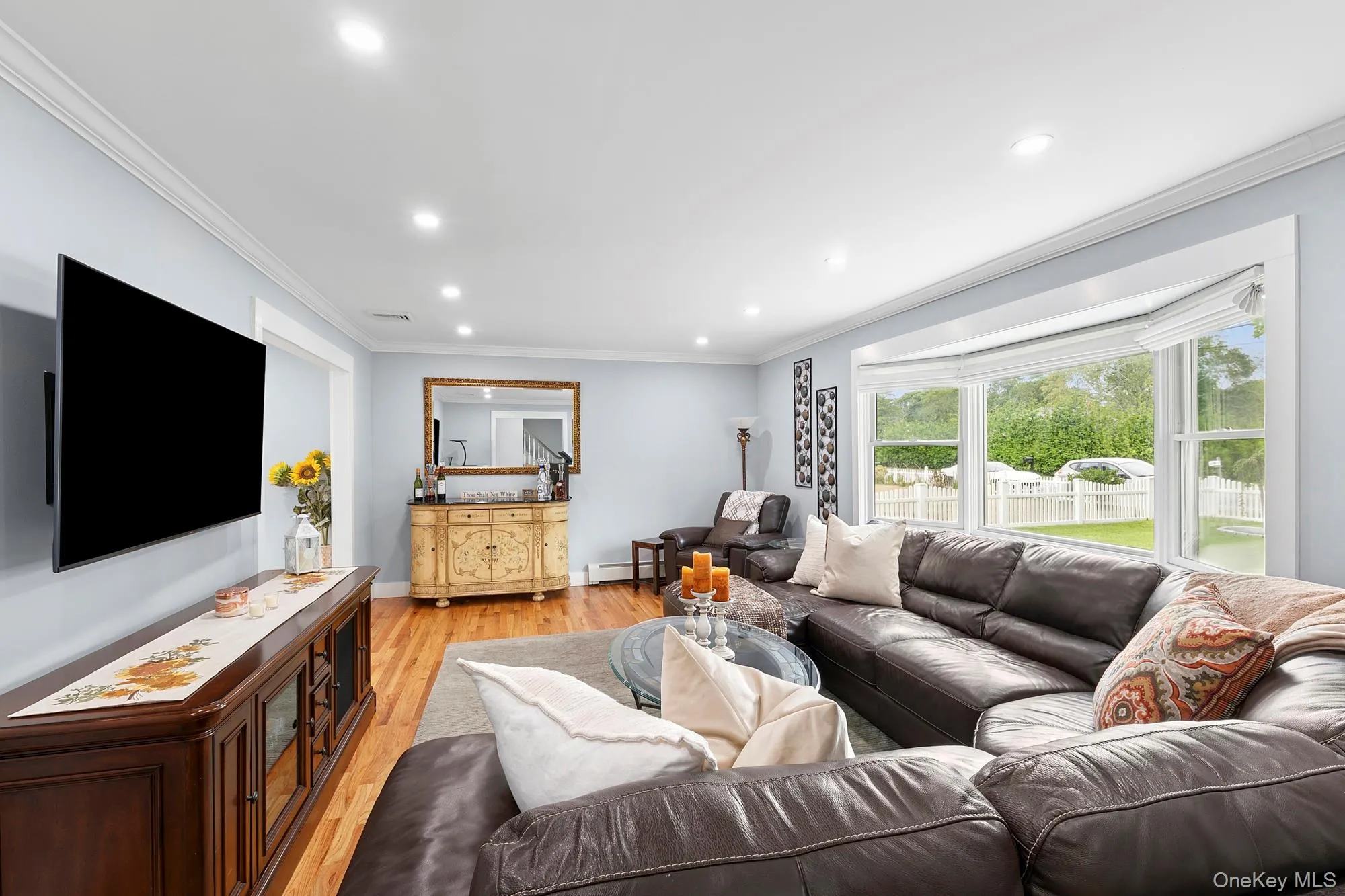 Living room with ornamental molding, light wood-style floors, recessed lighting, and a baseboard radiator Living room with ornamental molding, light wood-style floors, recessed lighting, and a baseboard radiator