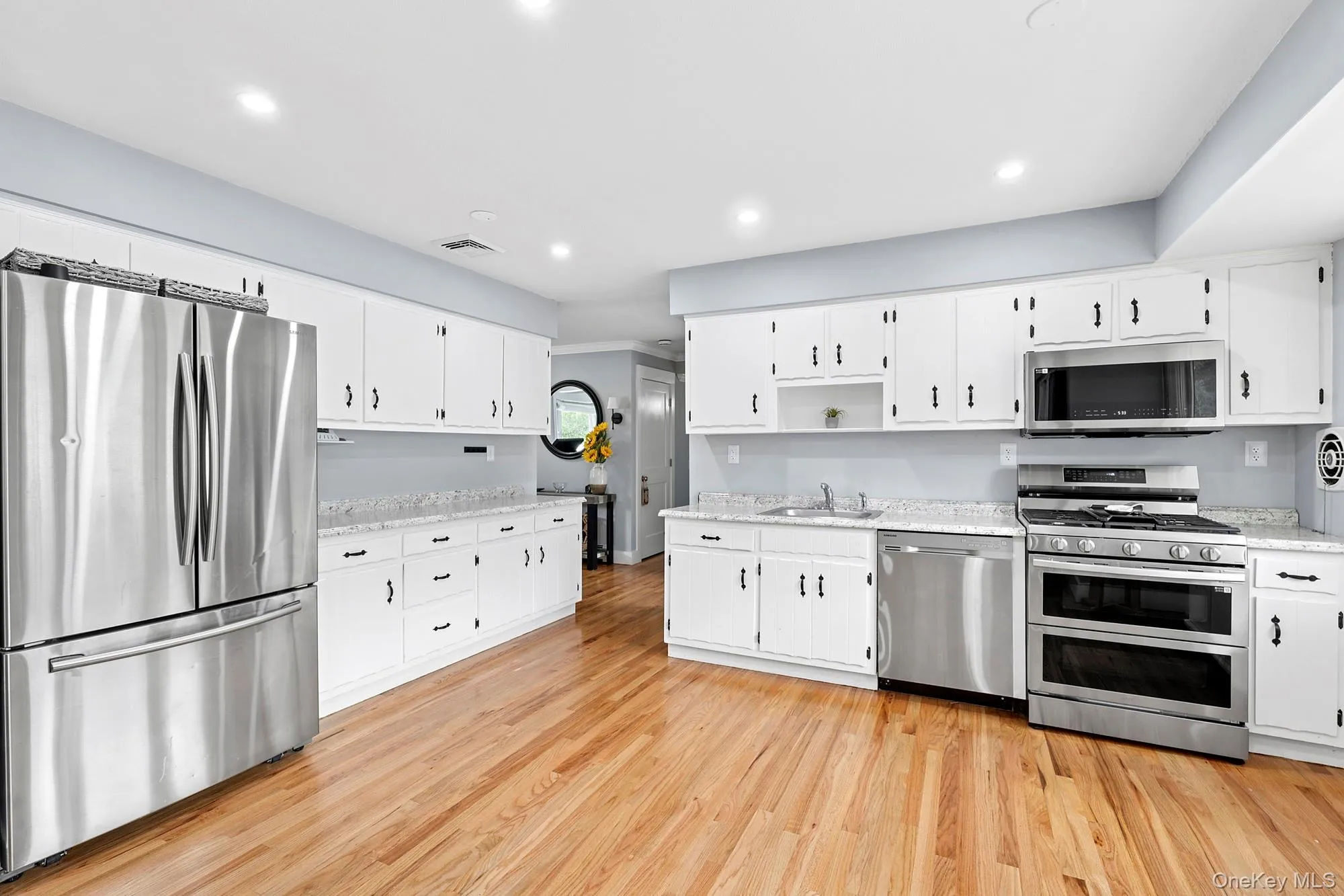 Kitchen with appliances with stainless steel finishes, white cabinetry, recessed lighting, light wood-type flooring, and open shelves Kitchen with appliances with stainless steel finishes, white cabinetry, recessed lighting, light wood-type flooring, and open shelves