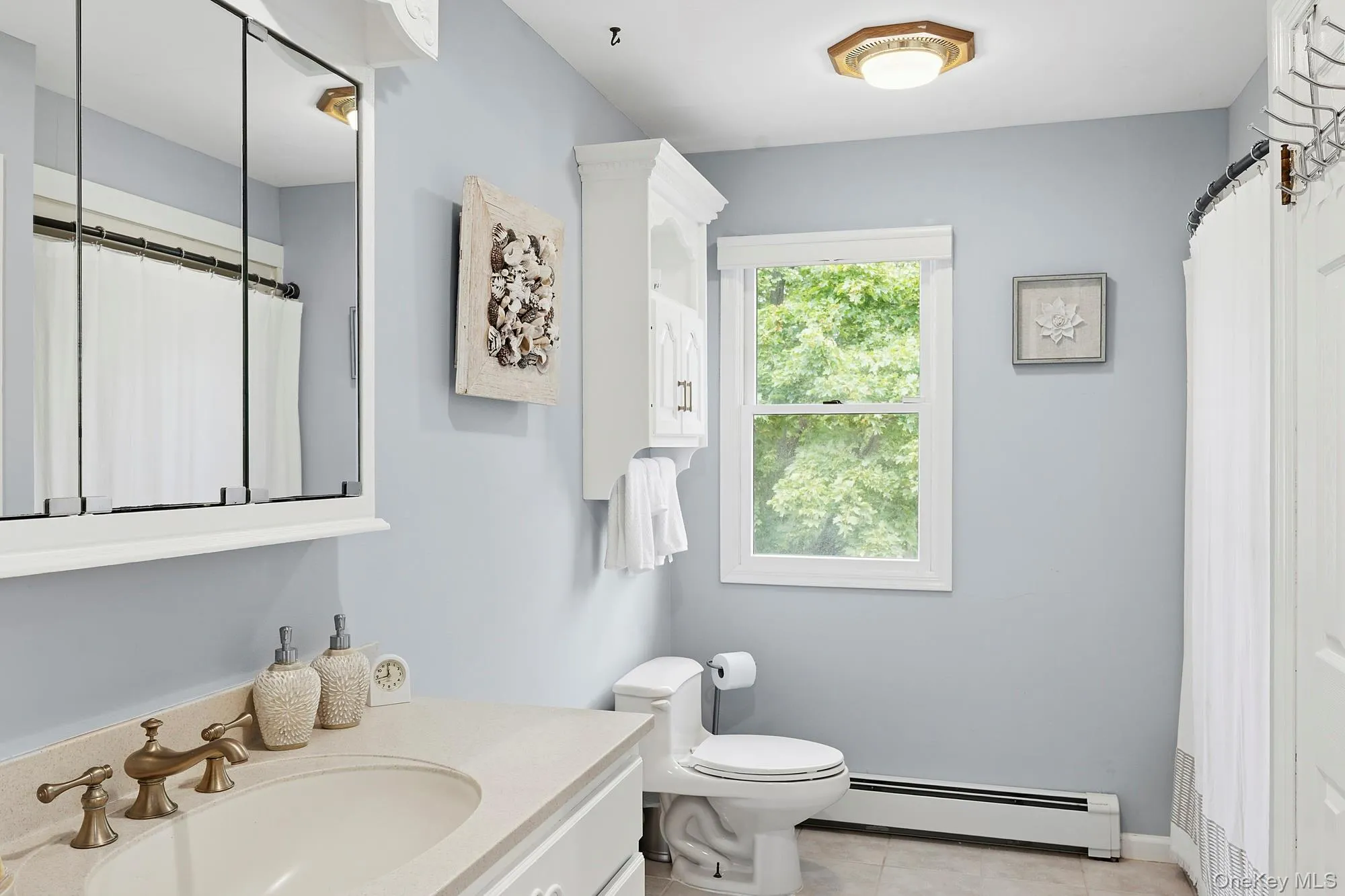 Full bath with a baseboard heating unit, light tile patterned floors, vanity, and curtained shower Full bath with a baseboard heating unit, light tile patterned floors, vanity, and curtained shower