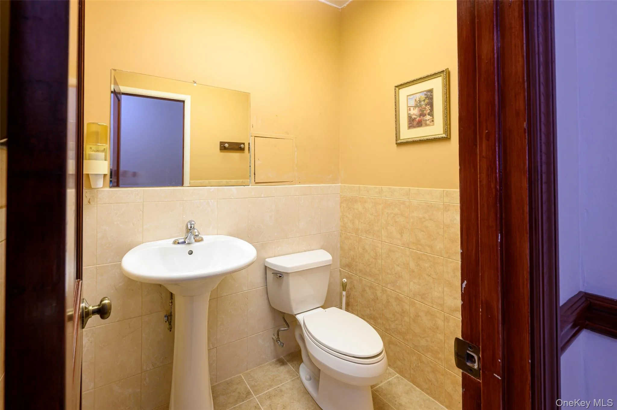 Bathroom with tile walls, toilet, a wainscoted wall, tile patterned floors, and a sink Bathroom with tile walls, toilet, a wainscoted wall, tile patterned floors, and a sink