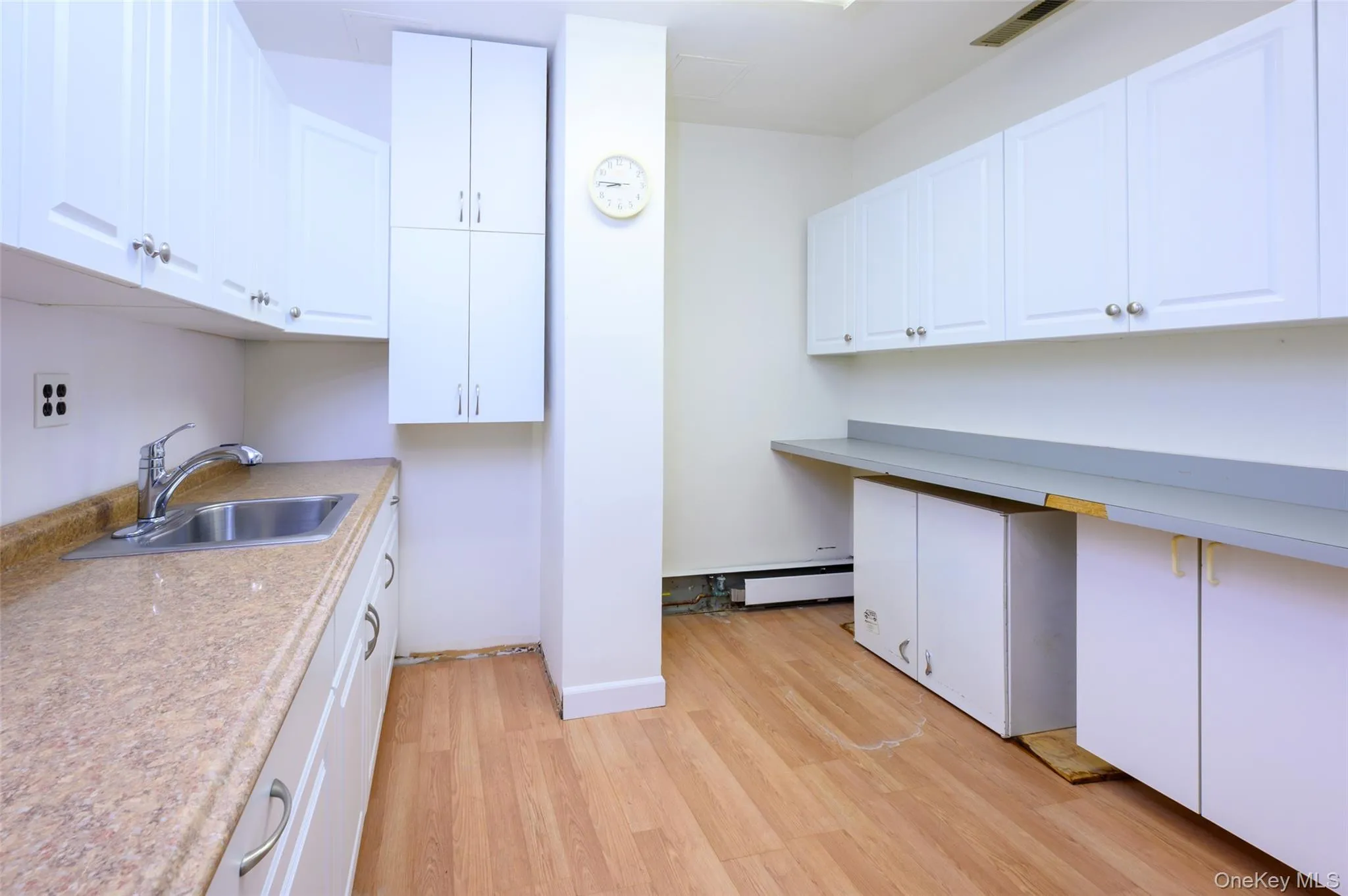 Kitchen with light wood finished floors, baseboard heating, white cabinets, and a sink Kitchen with light wood finished floors, baseboard heating, white cabinets, and a sink