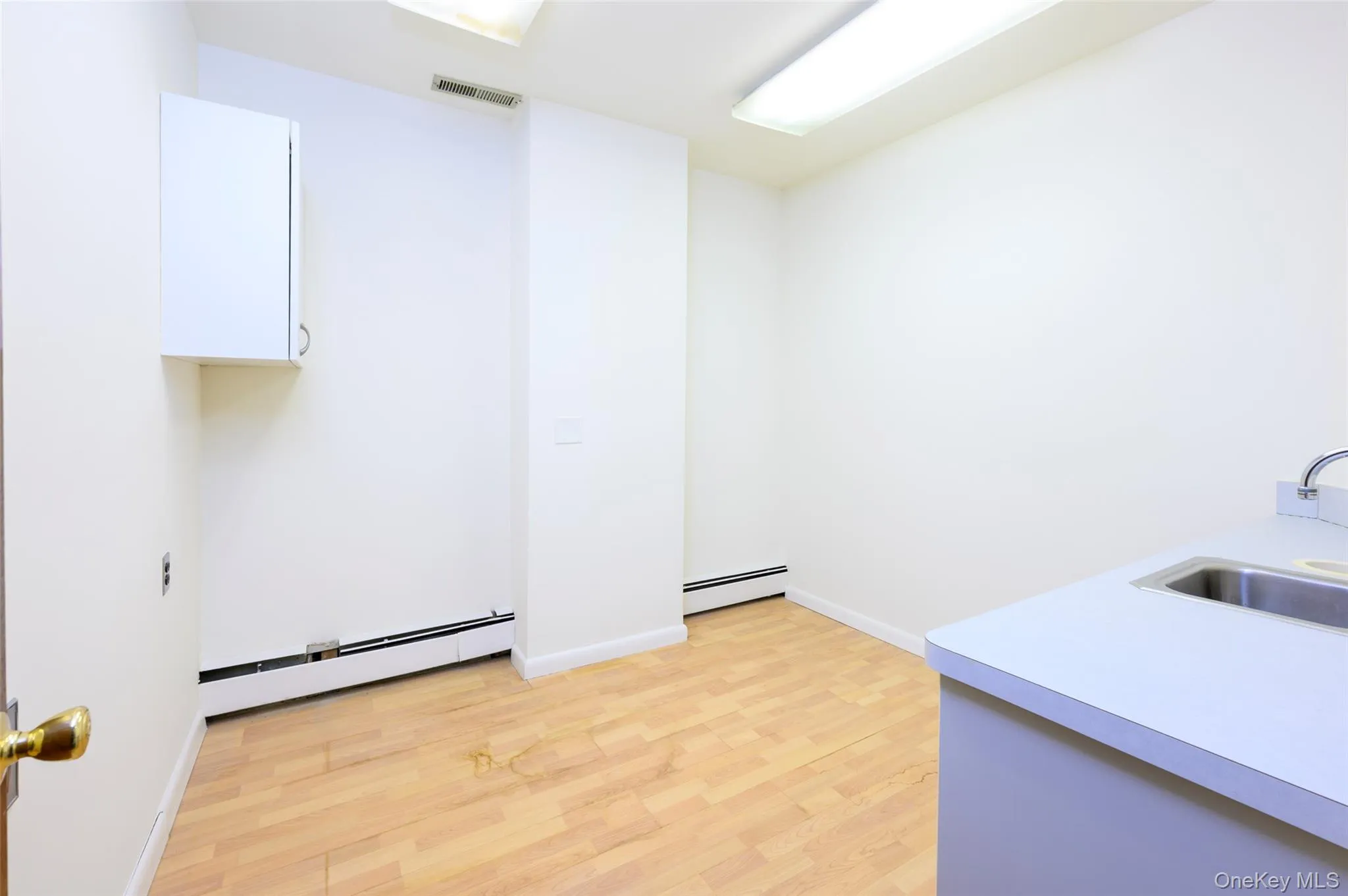 Clothes washing area with baseboard heating, a sink, visible vents, and light wood-style floors Clothes washing area with baseboard heating, a sink, visible vents, and light wood-style floors