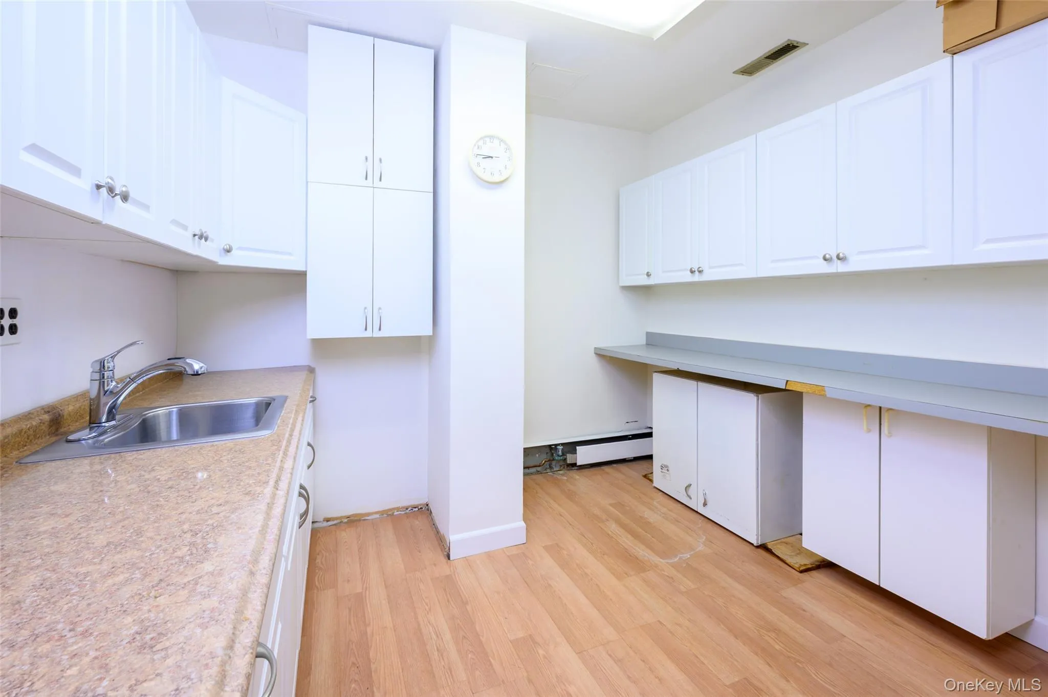 Kitchen featuring light countertops, a sink, light wood-style flooring, and white cabinetry Kitchen featuring light countertops, a sink, light wood-style flooring, and white cabinetry