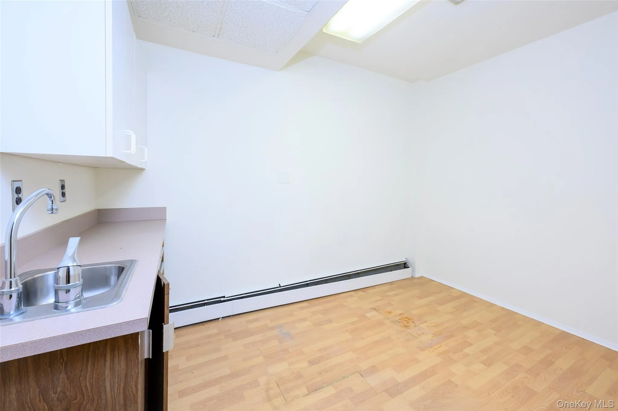 Kitchen featuring a baseboard radiator, a sink, white cabinetry, light countertops, and light wood-type flooring Kitchen featuring a baseboard radiator, a sink, white cabinetry, light countertops, and light wood-type flooring