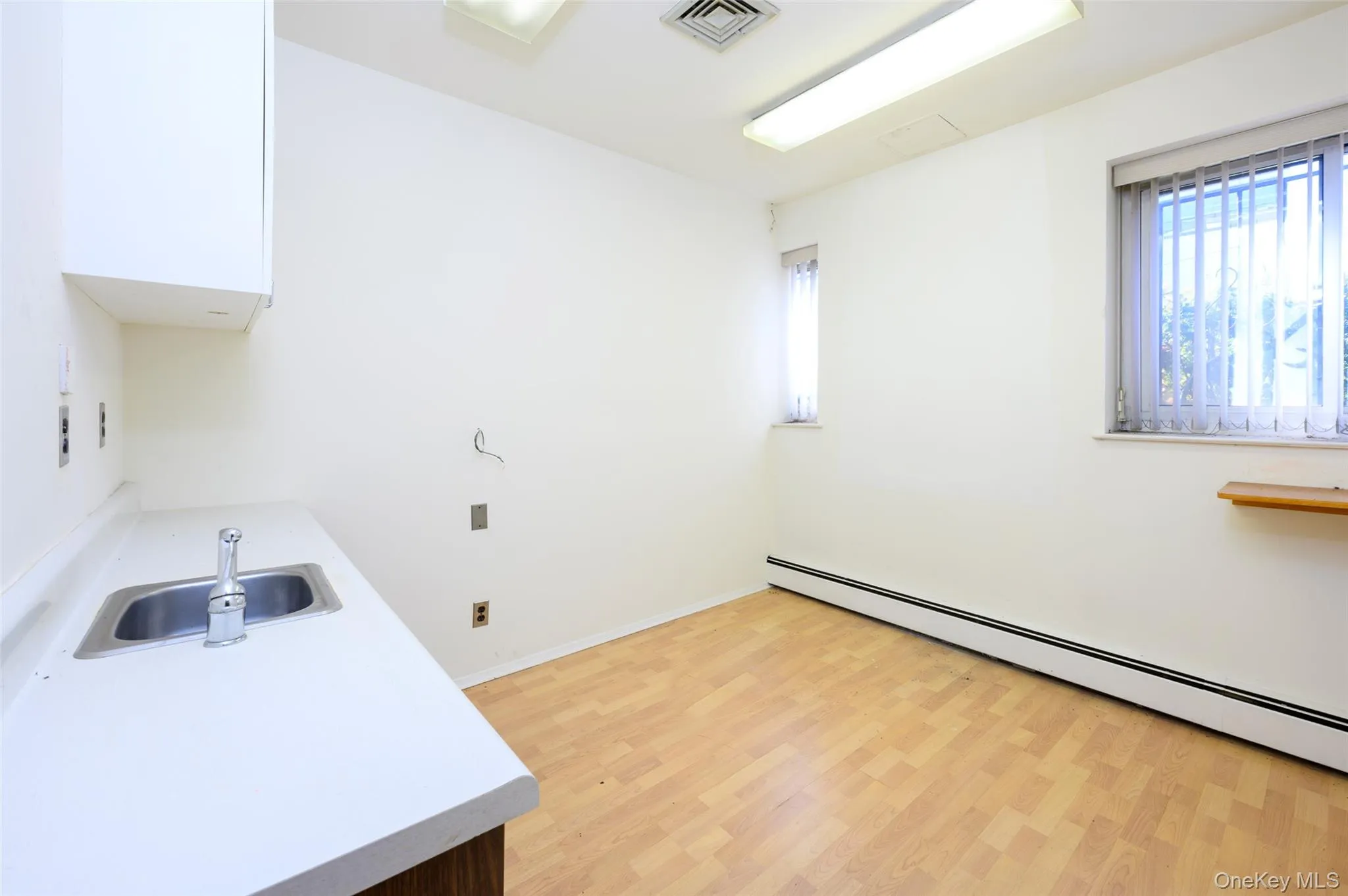 Kitchen with visible vents, light countertops, light wood-style floors, a baseboard heating unit, and a sink Kitchen with visible vents, light countertops, light wood-style floors, a baseboard heating unit, and a sink