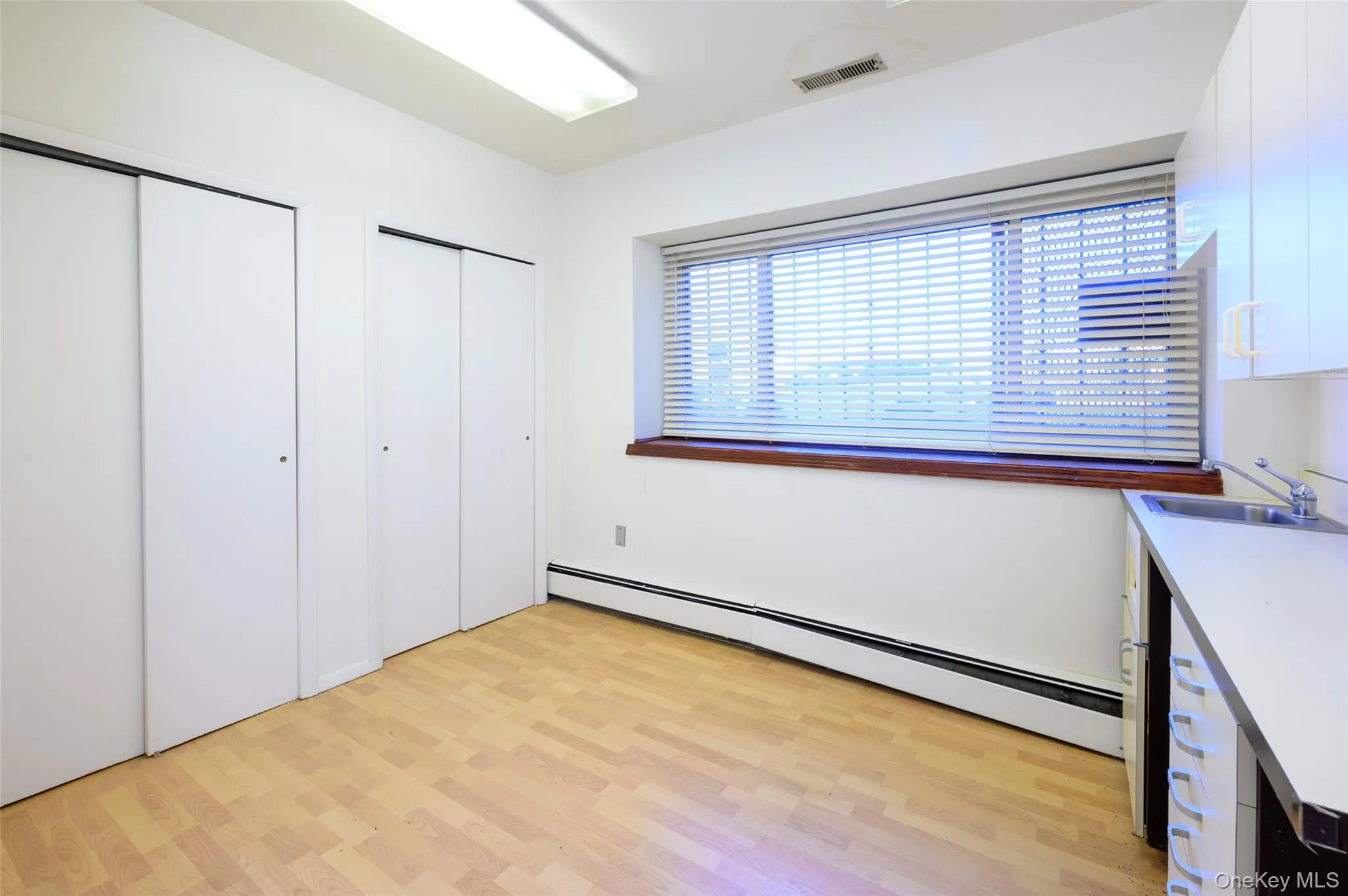 Unfurnished bedroom with visible vents, a baseboard radiator, a sink, light wood-style floors, and two closets Unfurnished bedroom with visible vents, a baseboard radiator, a sink, light wood-style floors, and two closets
