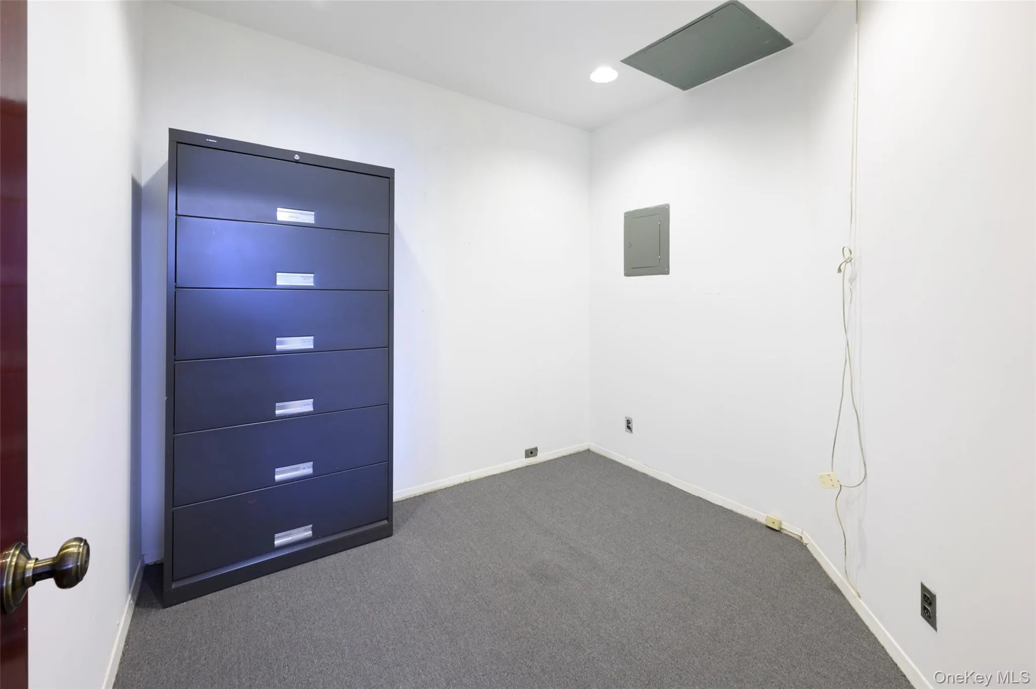 Empty room with dark colored carpet, recessed lighting, electric panel, and baseboards Empty room with dark colored carpet, recessed lighting, electric panel, and baseboards