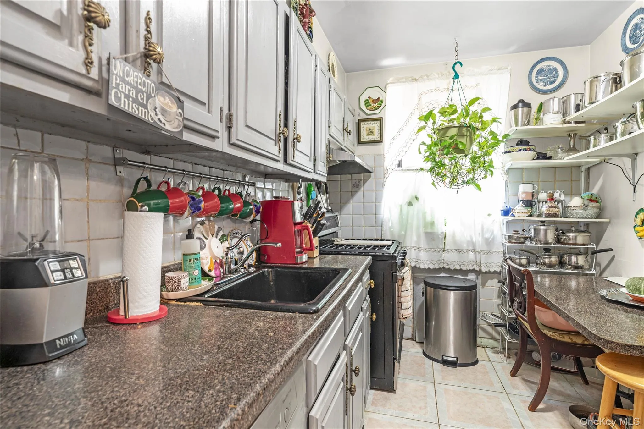 Kitchen featuring black gas range oven, light tile patterned floors, decorative backsplash, under cabinet range hood, and open shelves Kitchen featuring black gas range oven, light tile patterned floors, decorative backsplash, under cabinet range hood, and open shelves