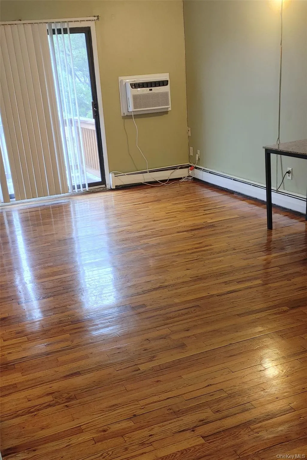 Unfurnished room with wood finished floors, a baseboard heating unit, and a wall unit AC Unfurnished room with wood finished floors, a baseboard heating unit, and a wall unit AC