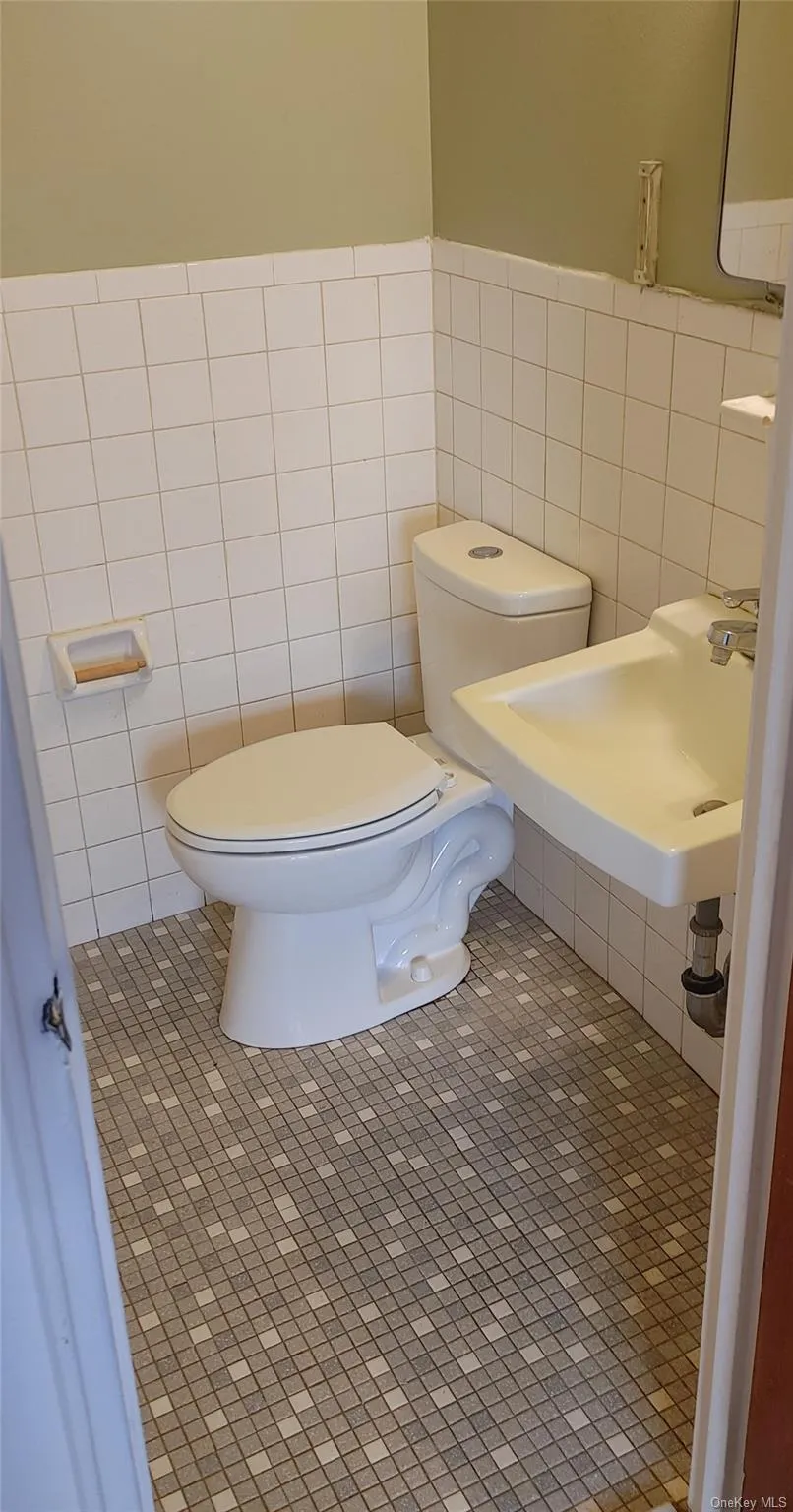 Half bathroom with tile patterned floors, tile walls, a sink, and toilet Half bathroom with tile patterned floors, tile walls, a sink, and toilet