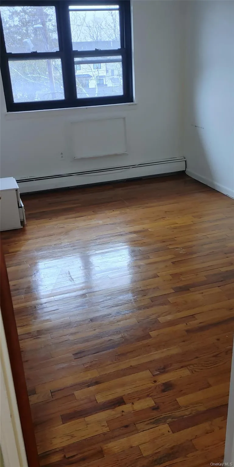 Empty room featuring a baseboard radiator and wood finished floors Empty room featuring a baseboard radiator and wood finished floors