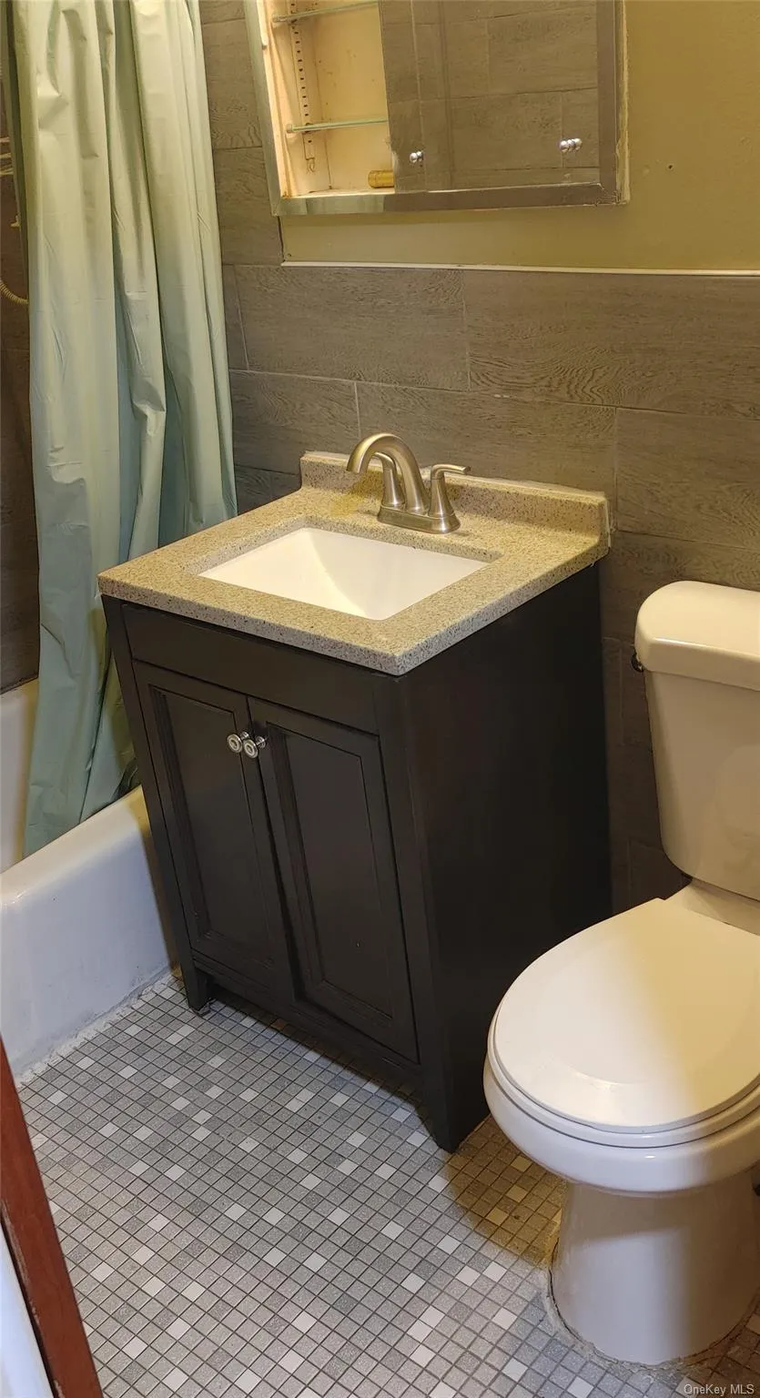 Full bath with toilet, vanity, shower / bath combination with curtain, and tile walls Full bath with toilet, vanity, shower / bath combination with curtain, and tile walls