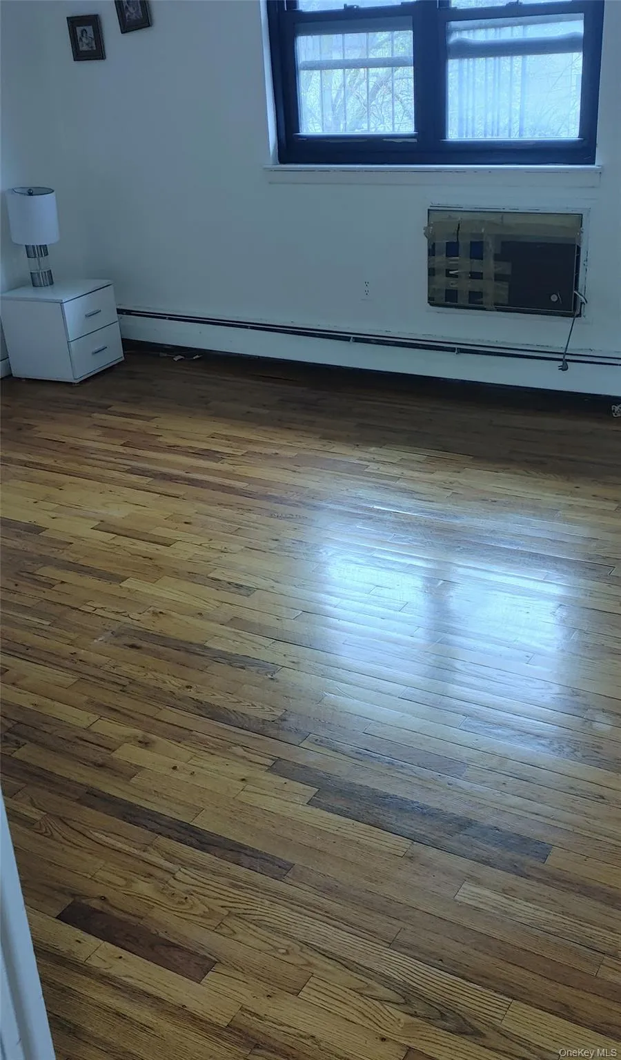Empty room with dark wood-style flooring and a baseboard heating unit Empty room with dark wood-style flooring and a baseboard heating unit