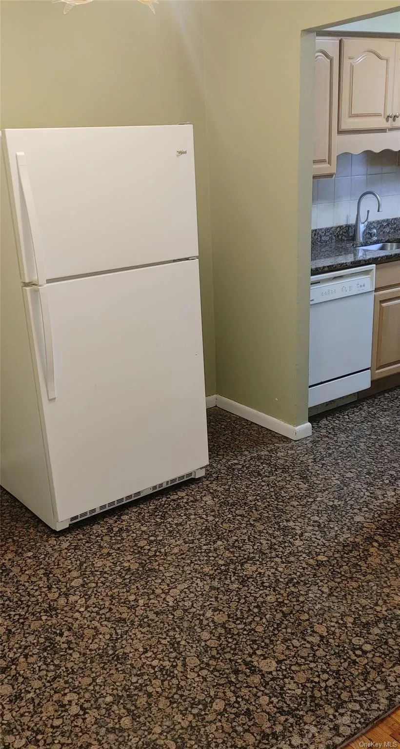 Kitchen featuring baseboards, white appliances, dark countertops, decorative backsplash, and a sink Kitchen featuring baseboards, white appliances, dark countertops, decorative backsplash, and a sink
