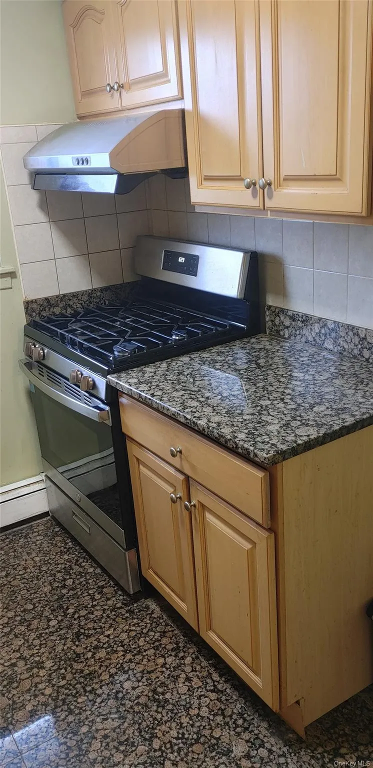 Kitchen featuring under cabinet range hood, stainless steel range with gas cooktop, dark stone counters, and decorative backsplash Kitchen featuring under cabinet range hood, stainless steel range with gas cooktop, dark stone counters, and decorative backsplash