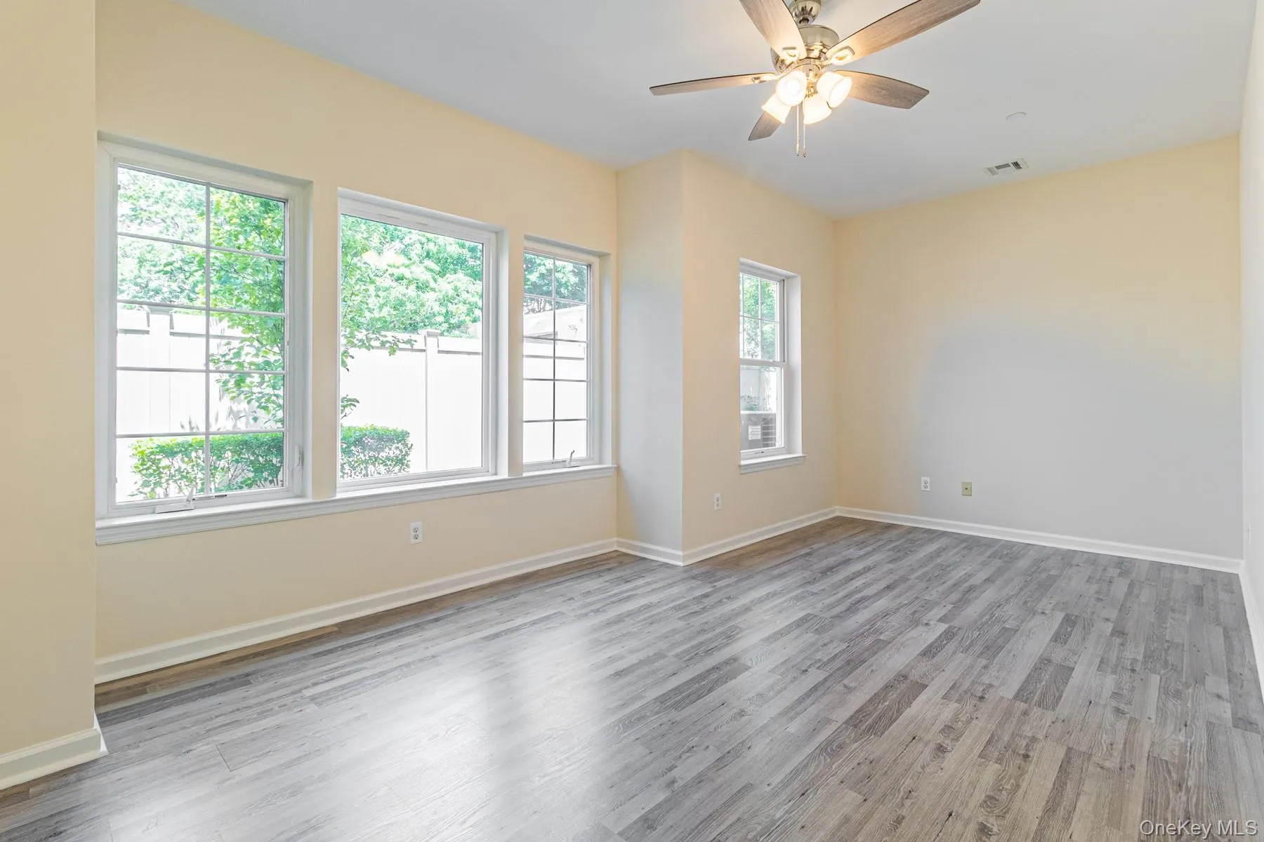 Empty room with a healthy amount of sunlight, wood finished floors, and visible vents Empty room with a healthy amount of sunlight, wood finished floors, and visible vents